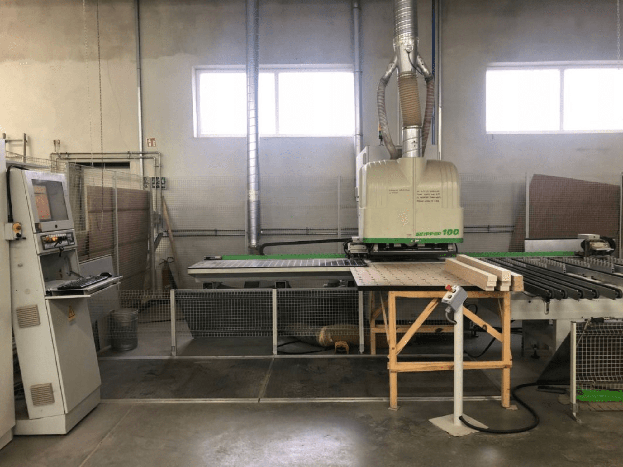 CNC obráběcí centrum BIESSE SKIPPER 100 v dílně; na předním pohledu je vidět stroj s ovládacím panelem a dřevem na stole.