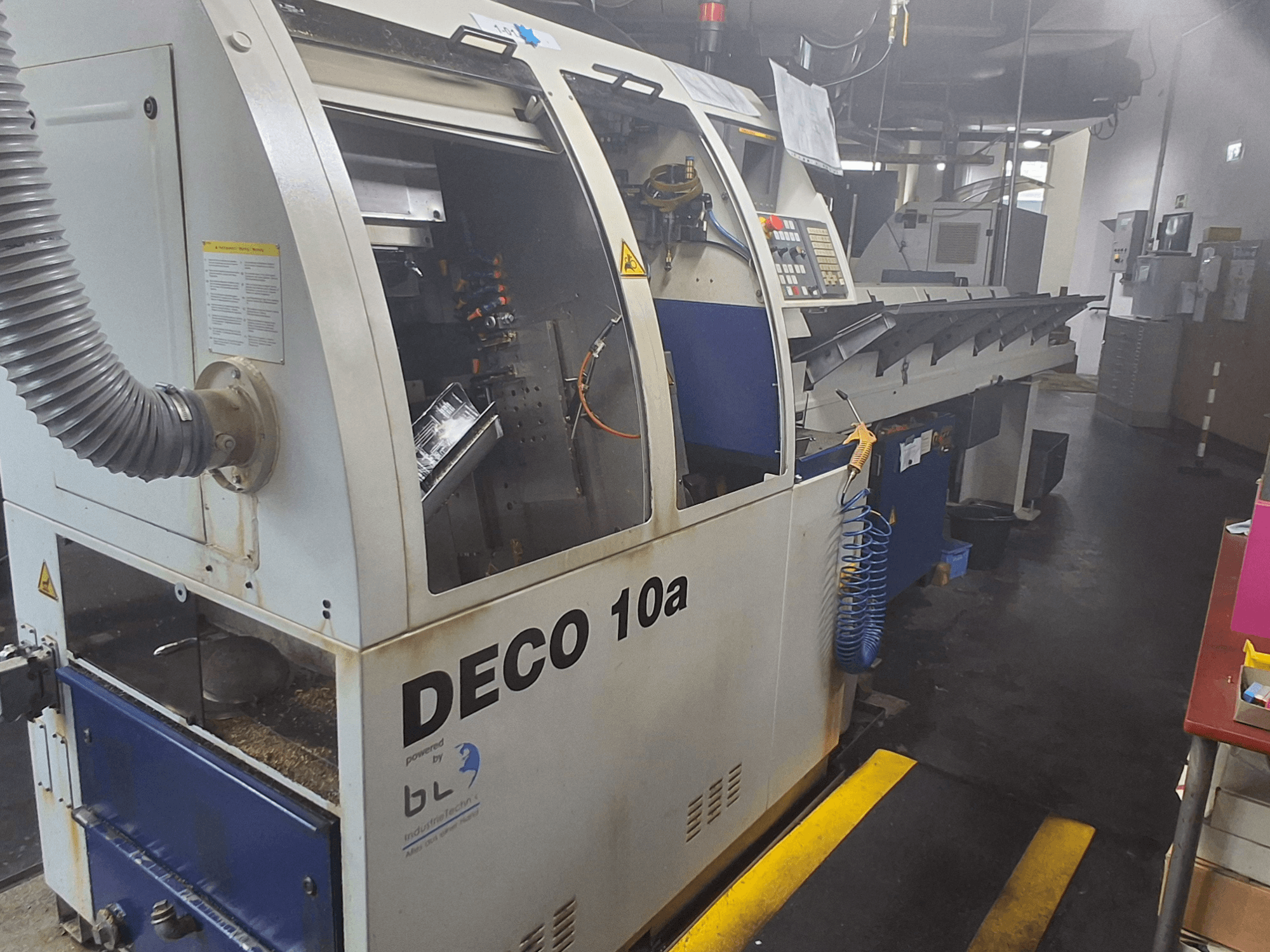 Soustruh švýcarského typu TORNOS DECO 10a, pohled zepředu; má ovládací panel, viditelné mechanismy a trubku pro odsávání prachu.