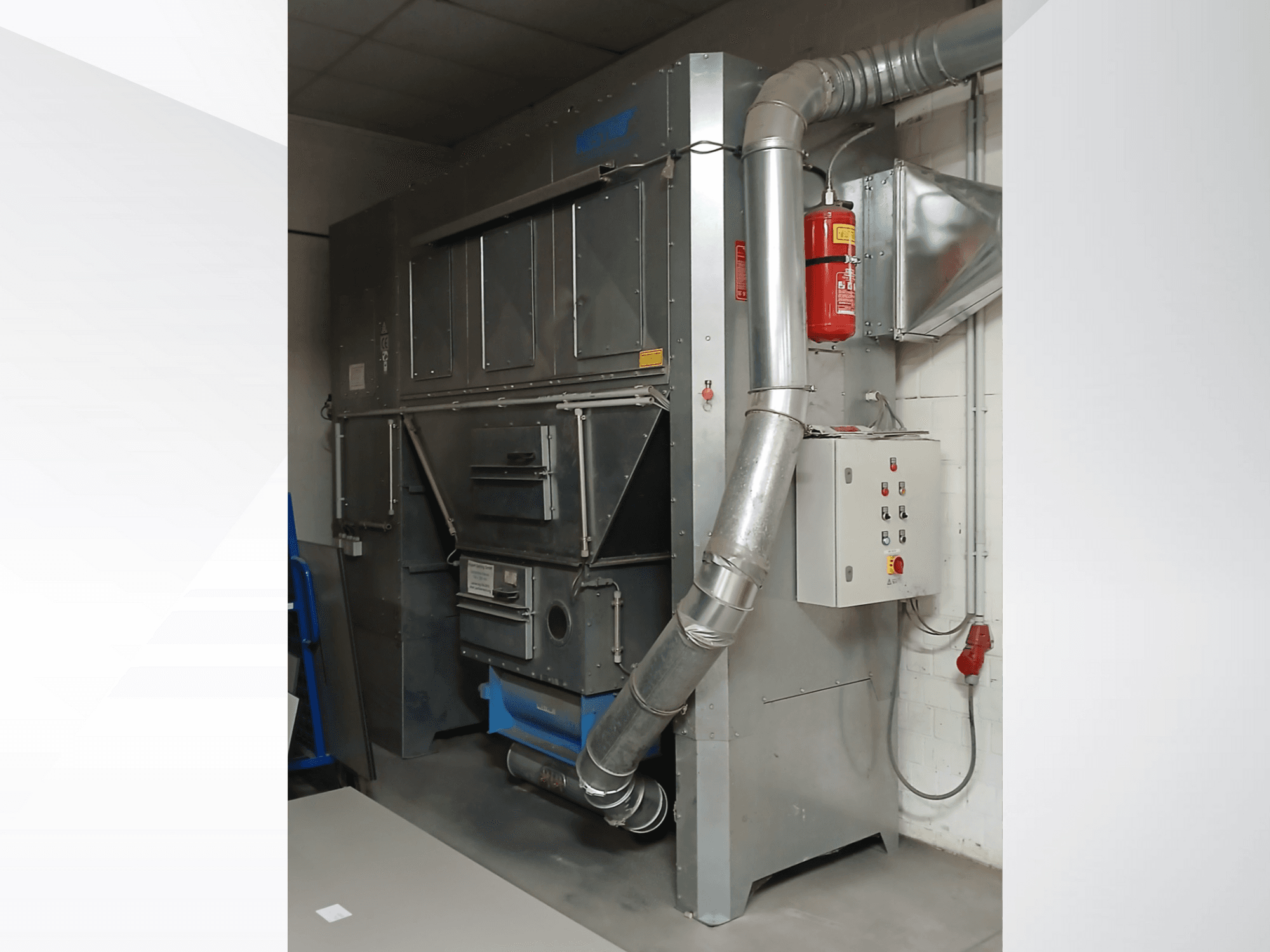 Průmyslový odlučovač prachu, šedý kov, pohled zepředu; obsahuje výfukové potrubí, ovládací panel a hasicí přístroj.