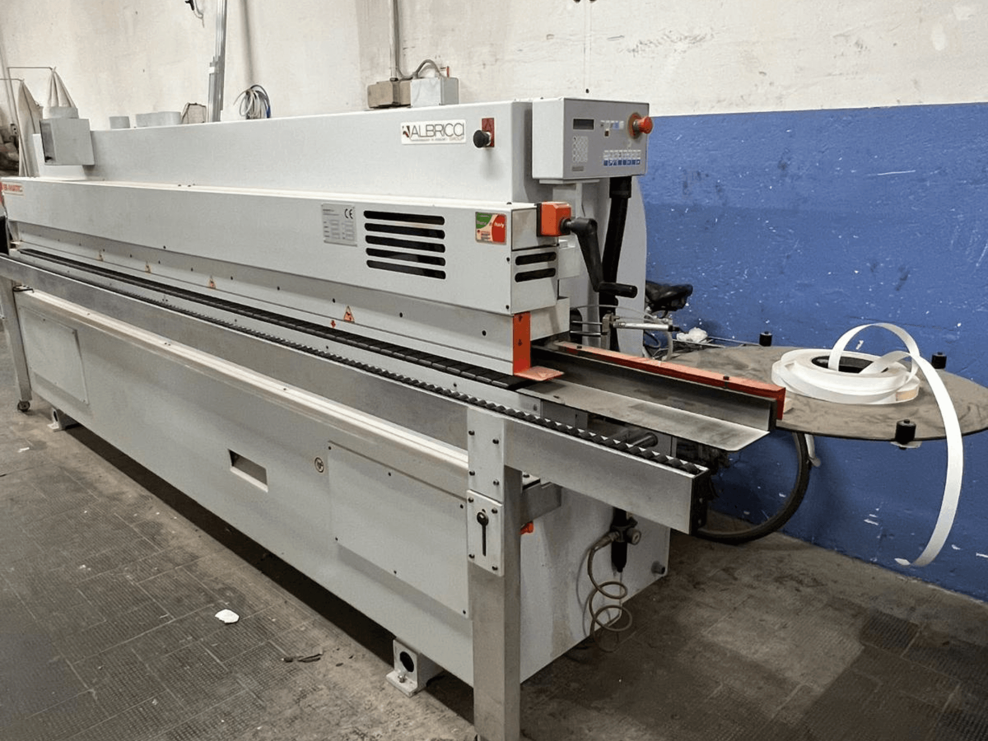 Olepovačka hran ALBRICO s pohledem zepředu, s dlouhým dopravním pásem a připojenou rolí lepicí pásky.