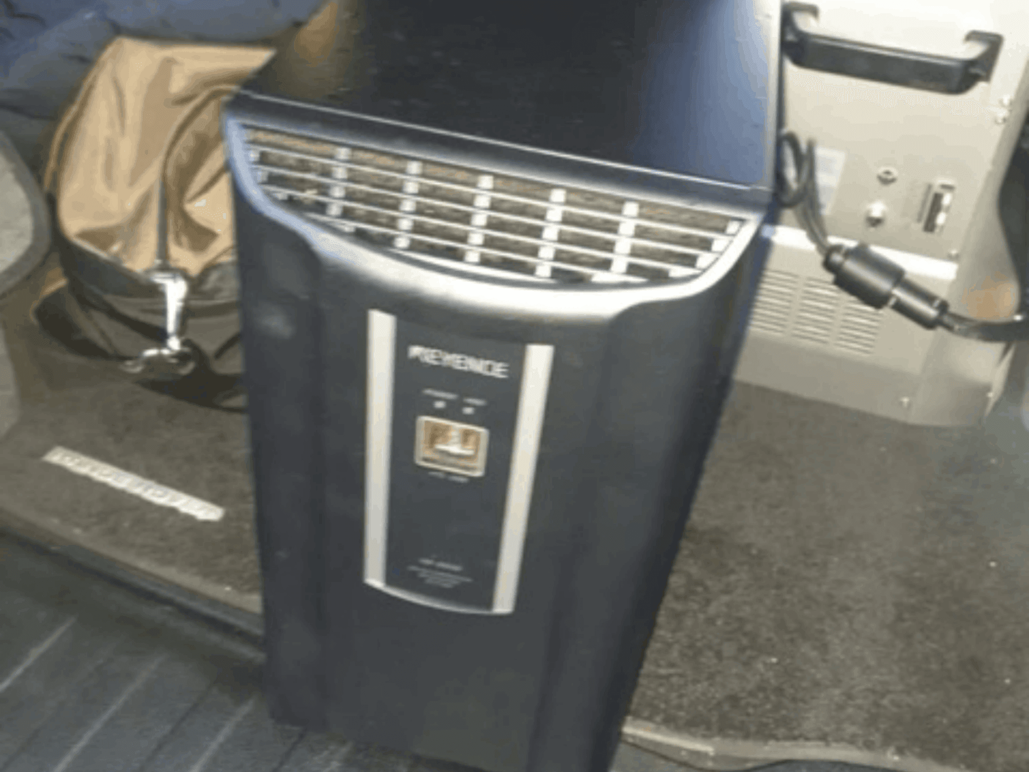 Automatizační systém KEYENCE IM-8030 v čelním pohledu, na kterém je vidět ovládací panel a ventilační otvory na pozadí interiéru vozidla.