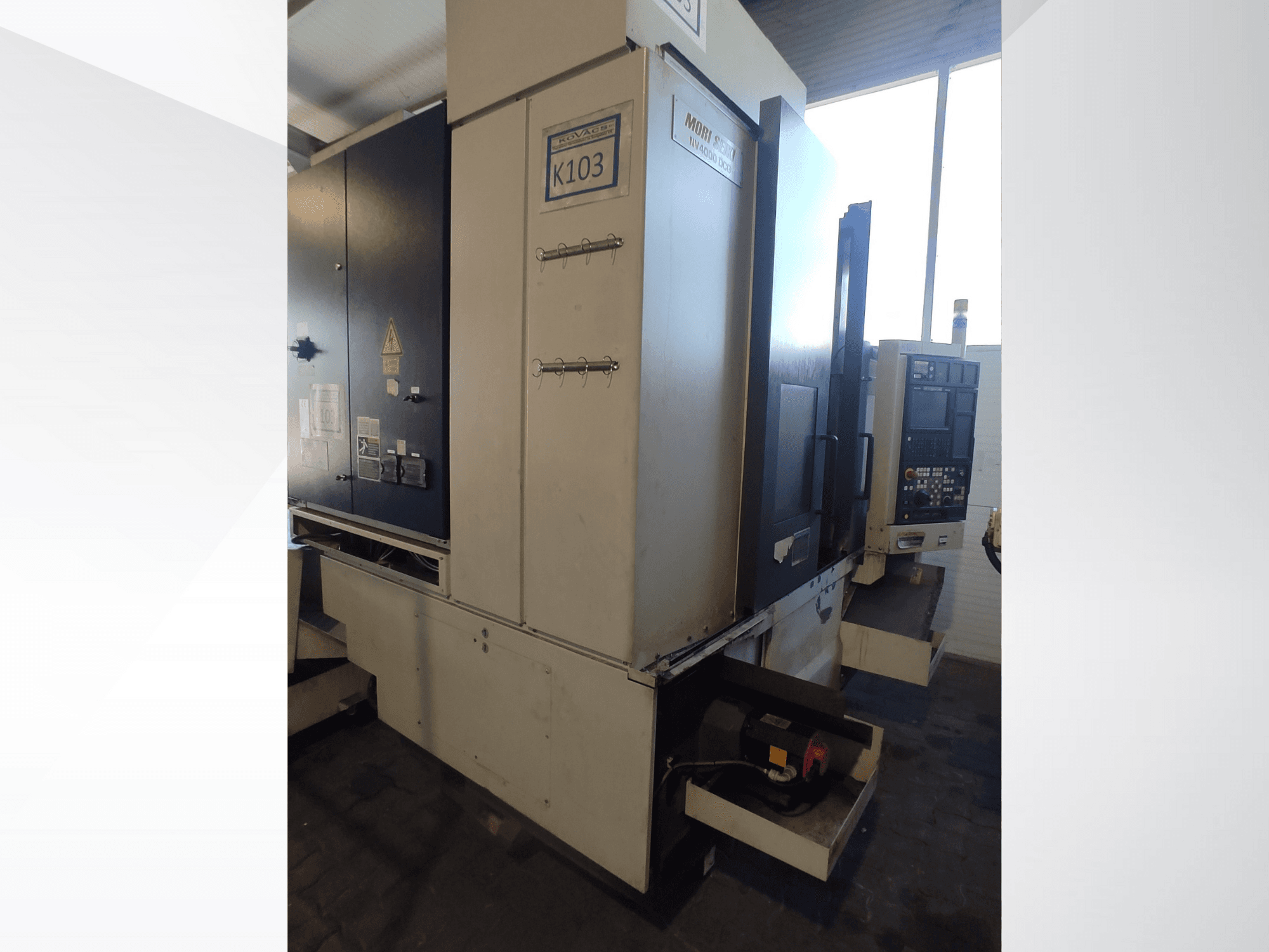 Stroj Mori Seiki K103 CNC v čelním pohledu, s viditelným ovládacím panelem, bezpečnostními štítky a elektrickými součástmi.