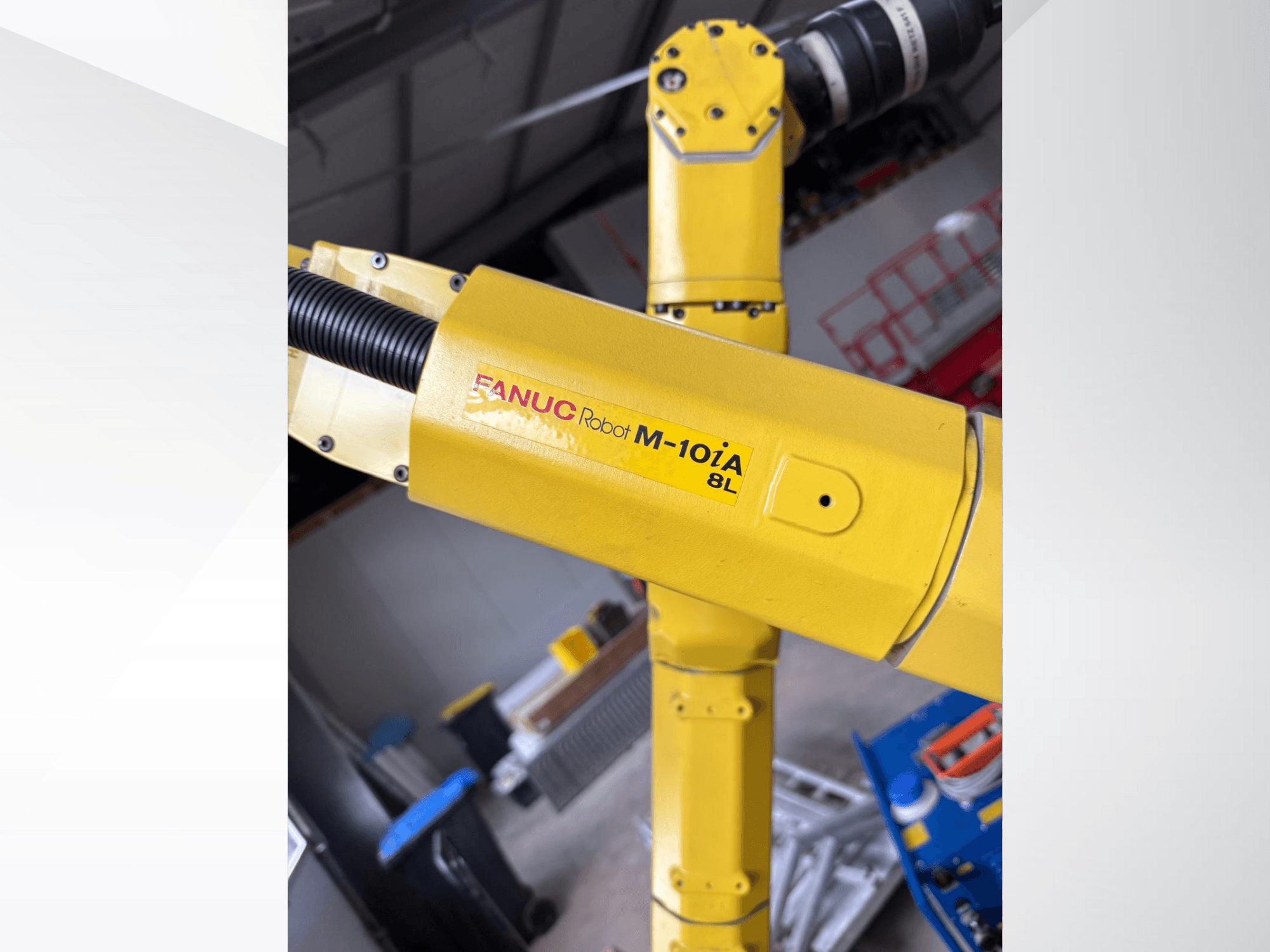 Robot FANUC M-10iA 8L ve žluté barvě, pohled z boku, ukazuje kloub ramene a mechanické součásti v průmyslovém prostředí.