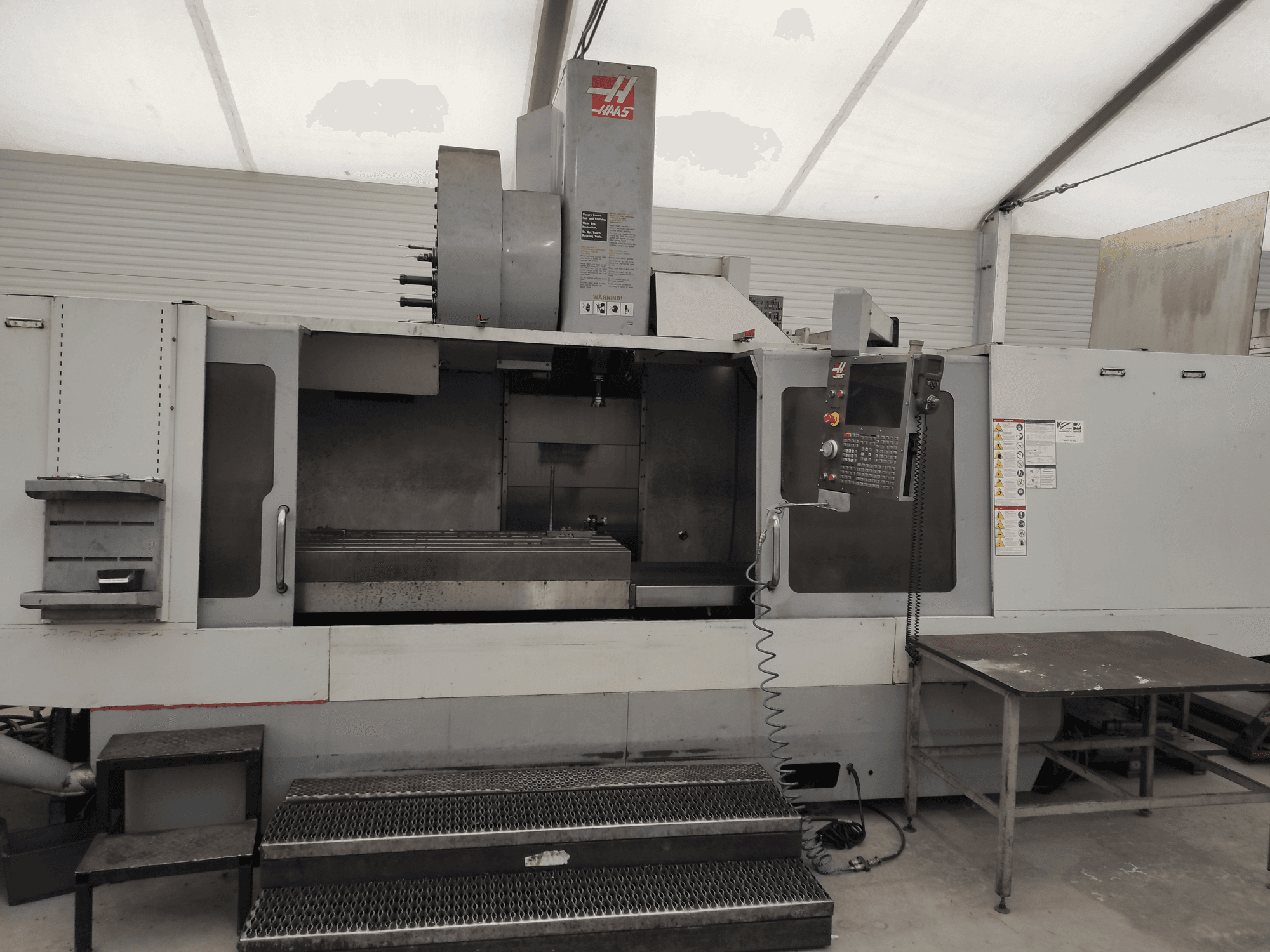 Vertikální obráběcí centrum HAAS VF-10/50HE, čelní pohled zobrazující ovládací panel, lože stroje a přístupný schod pro obsluhu.