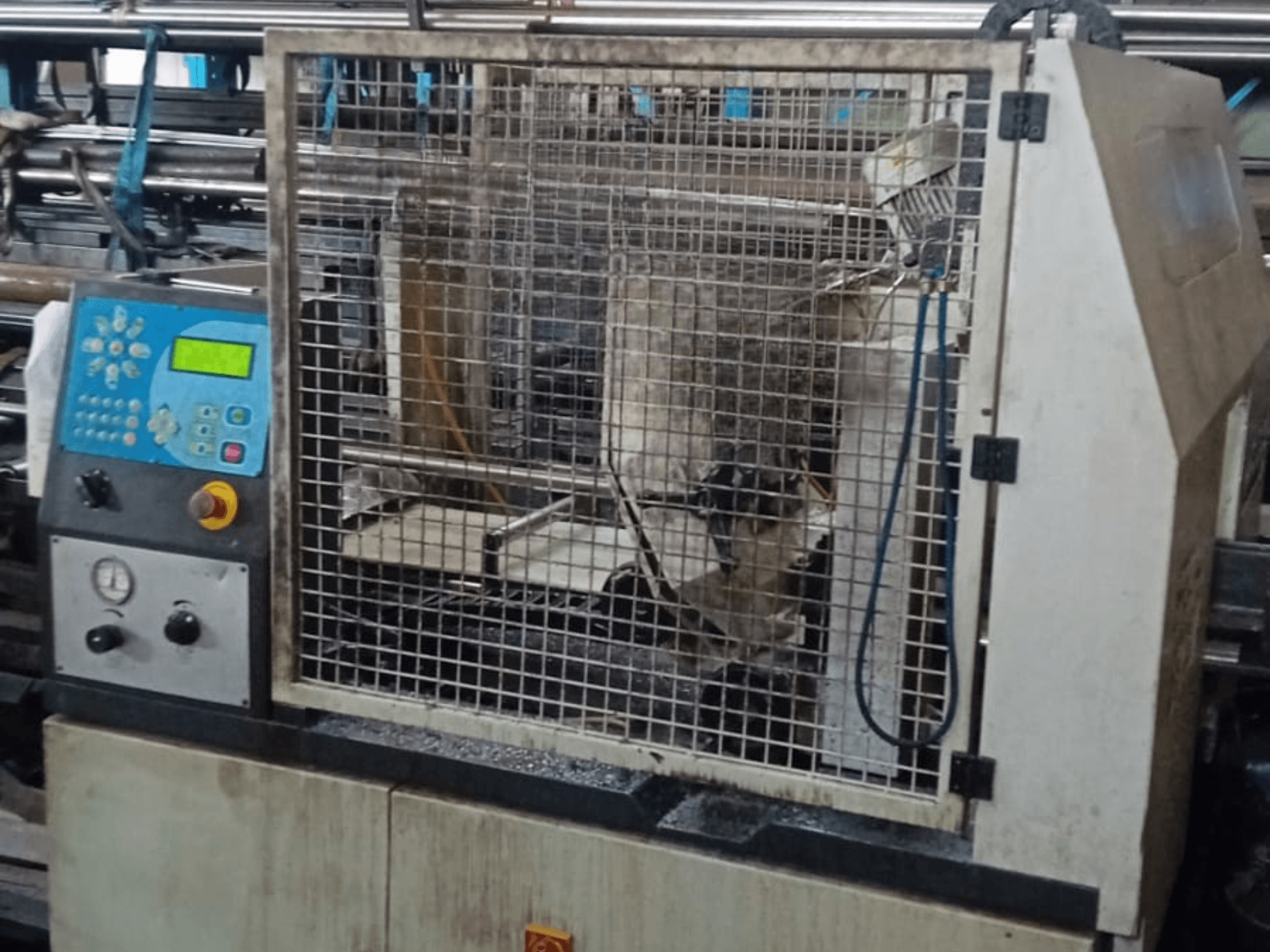 Pásová pila na kov Macc 381 AV, pohled zepředu, zobrazující ovládací panel, bezpečnostní klec a zbytky kovu na základně.