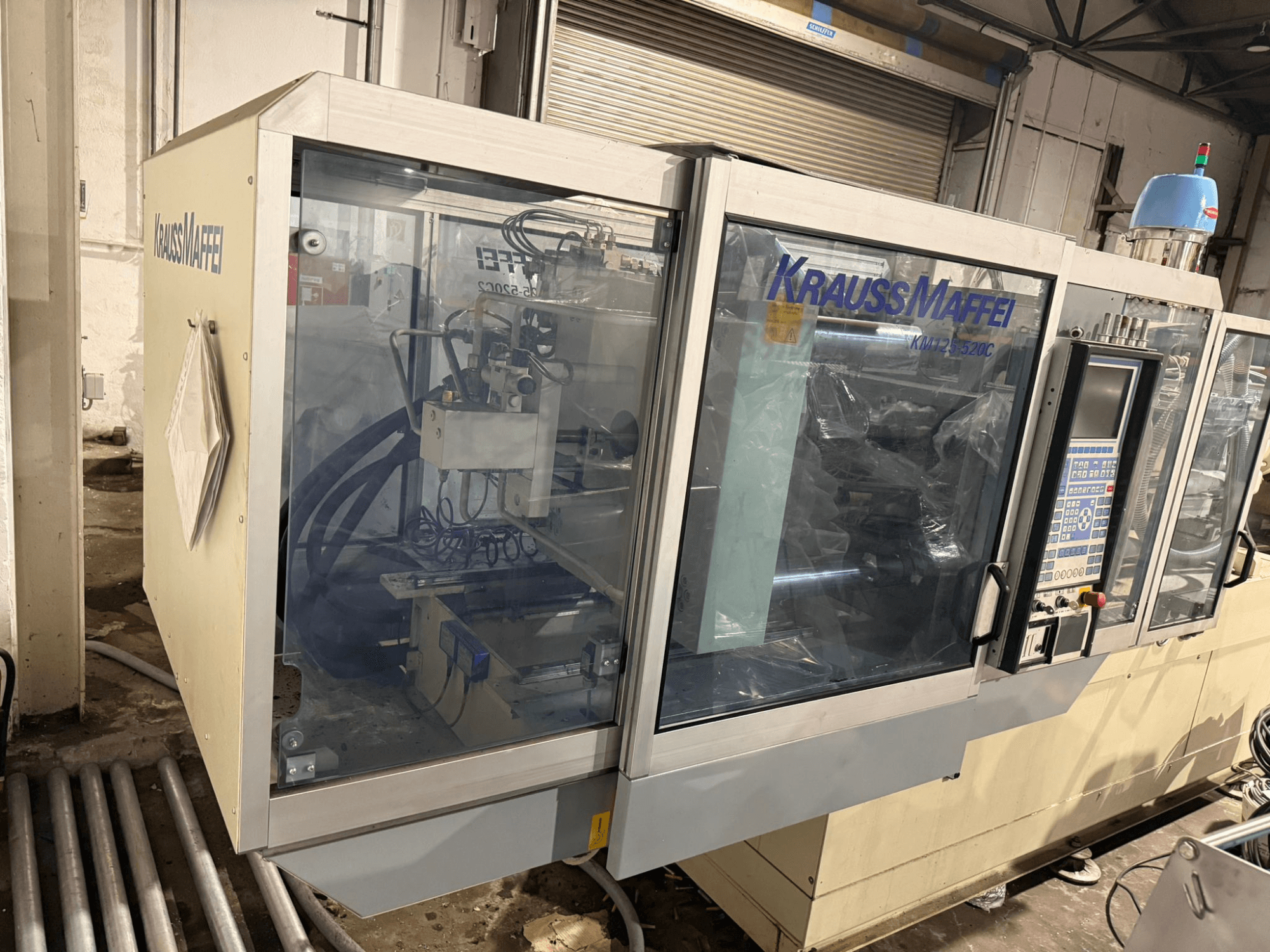 Hydraulický vstřikovací stroj Krauss Maffei KM125-520C2, čelní pohled s ovládacím panelem a průhledným krytem.