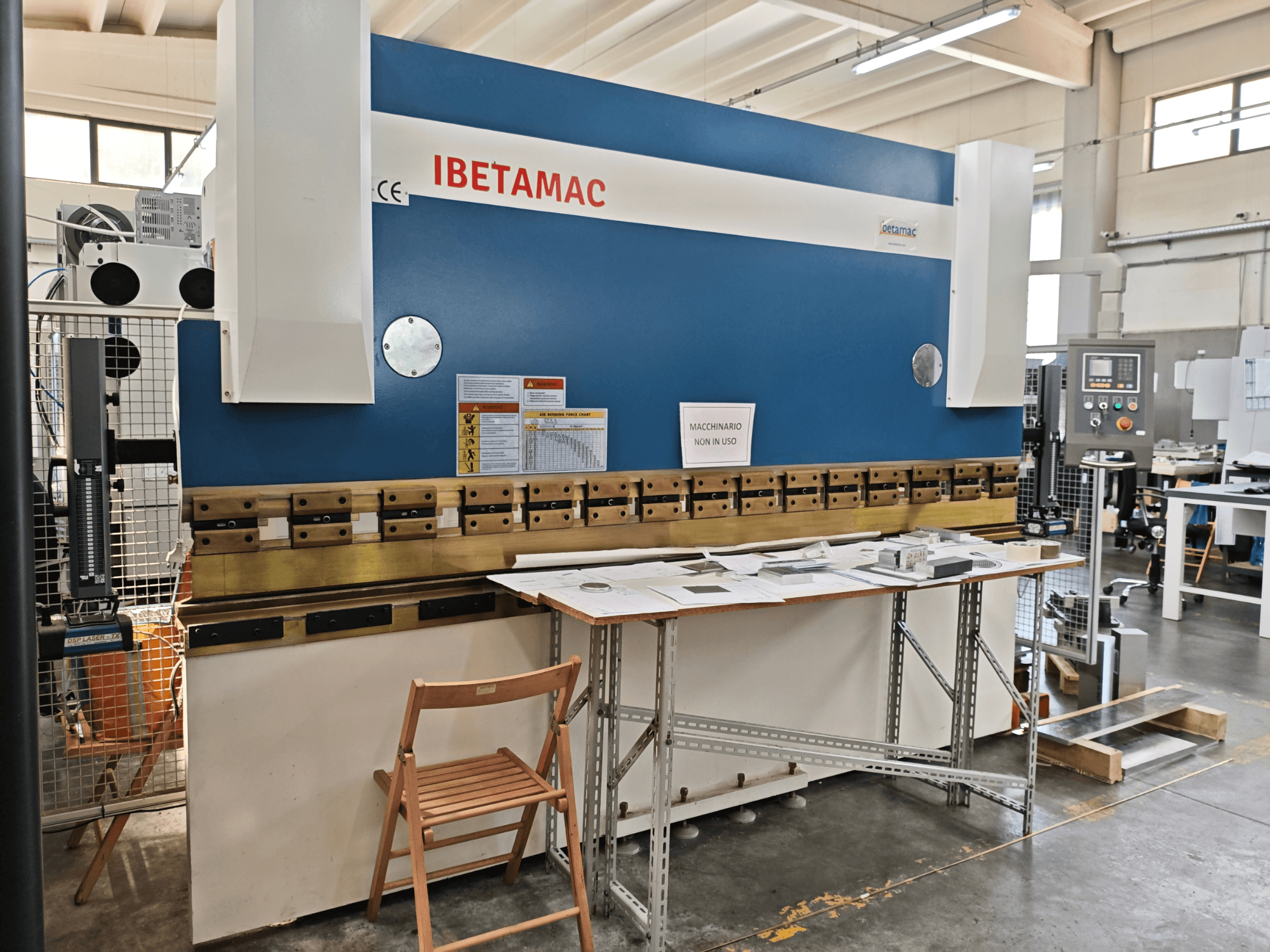 Ohýbačka IBETAMAC 3200 100T v dílně, boční pohled znázorňující ovládací panel, pracovní prostor a bezpečnostní pokyny.