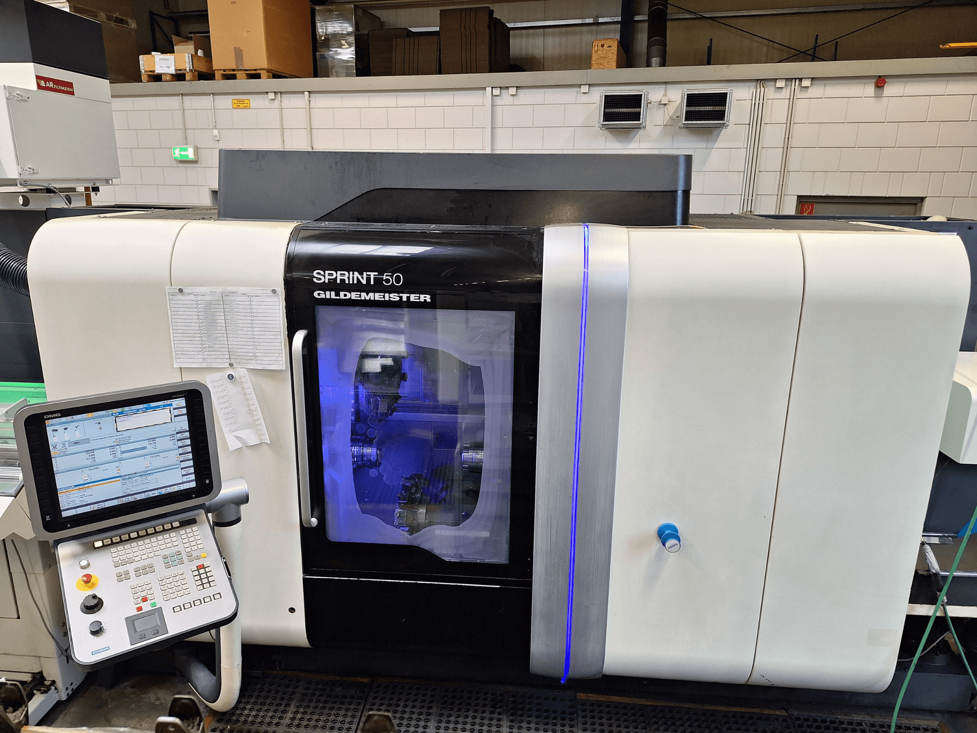 Horizontální soustruh DMG Sprint 50 2T, pohled zepředu, s ovládacím panelem a průhledným krytem, který ukazuje strojní zařízení uvnitř.