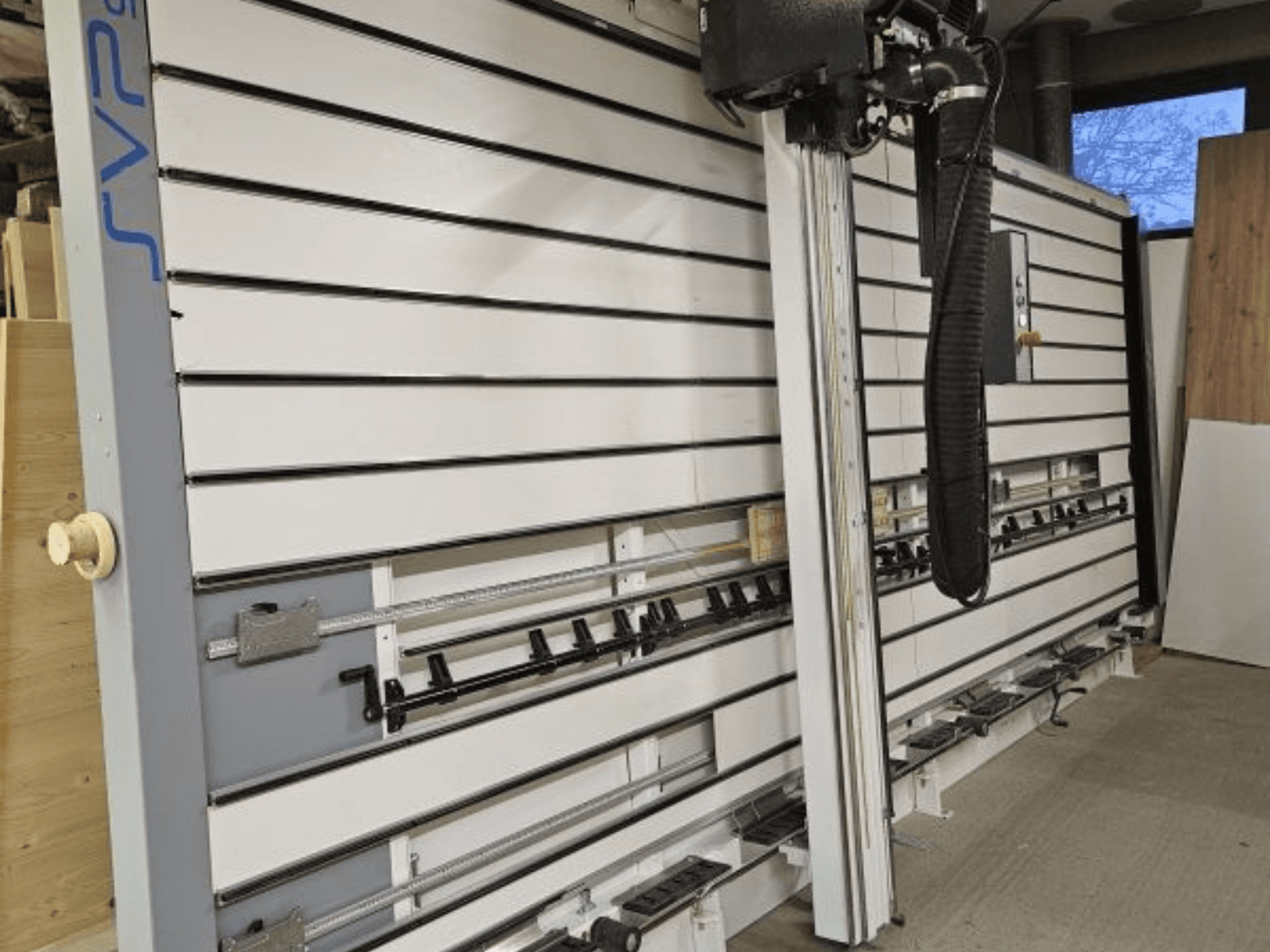 Posuvná desková pila SVP v dílně, pohled zepředu, s nastavitelnými pásy a horním systémem odsávání prachu.