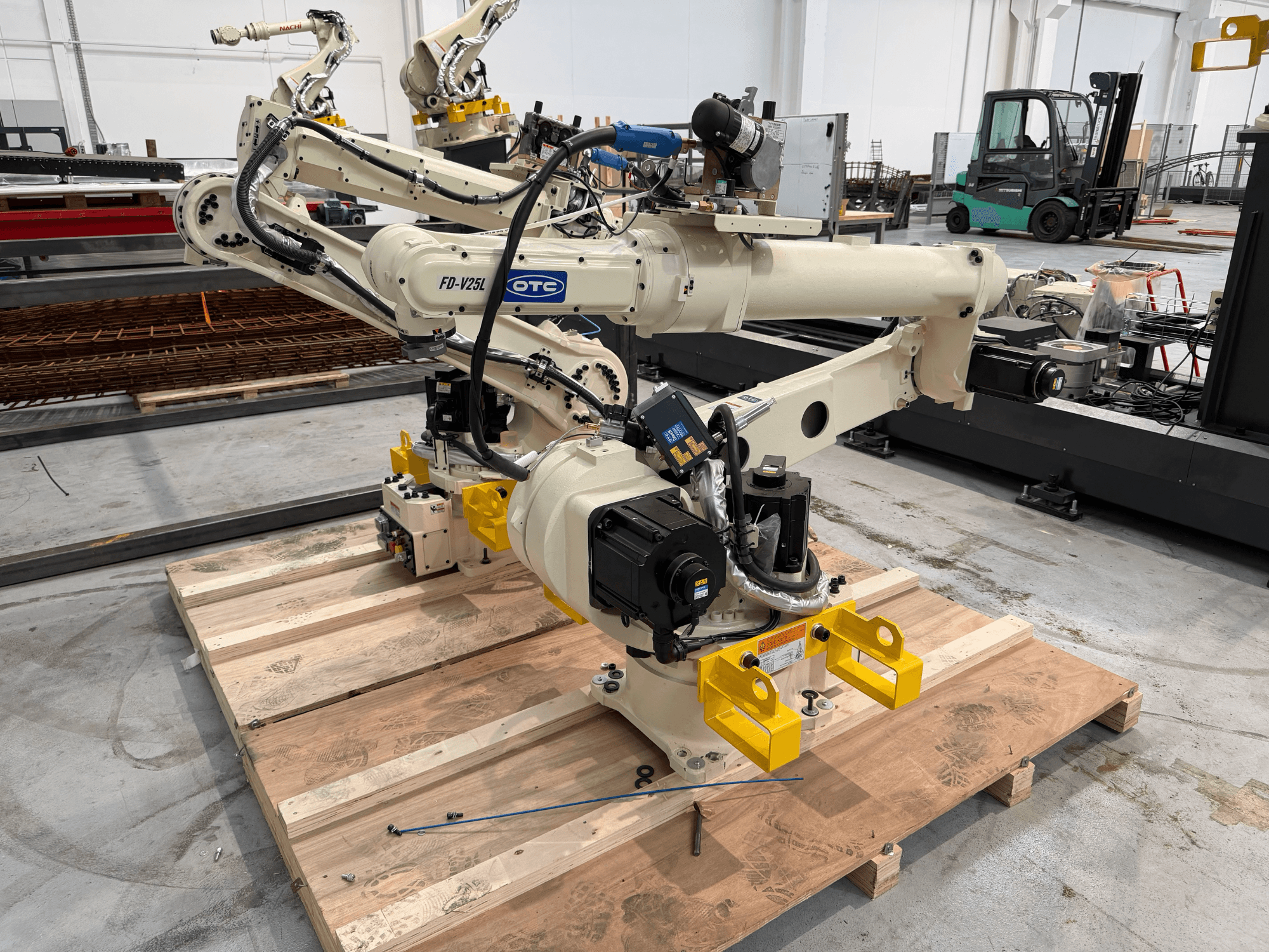 Robotické rameno OTC Daihen FD19-V25L v čelním pohledu, se žlutými chapadly a viditelnými mechanickými součástmi, umístěné na dřevěné paletě.