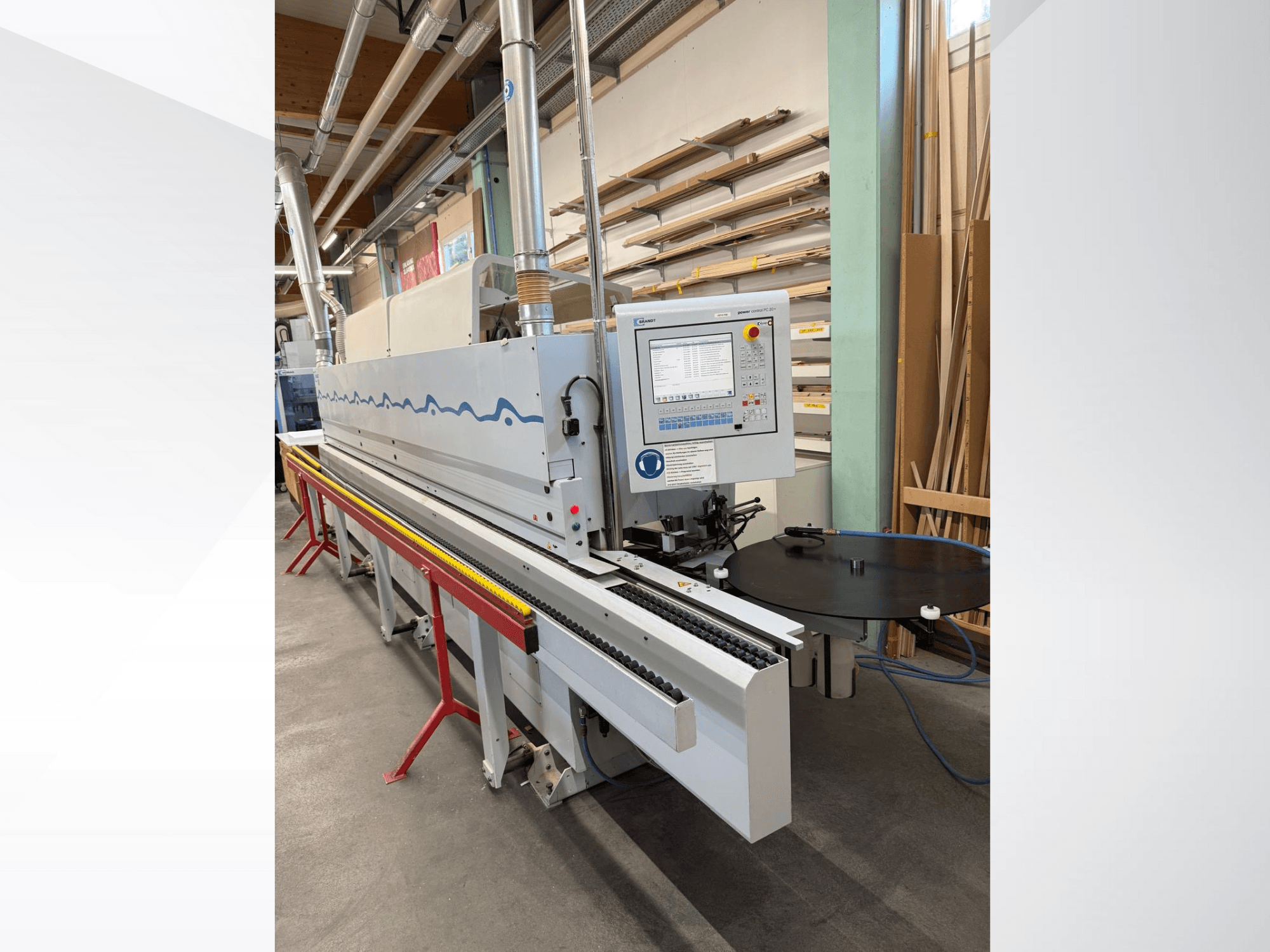 Pohled zepředu na automatický olepovací stroj HolzHer s ovládacím panelem, dopravním systémem a kulatým opěrným stolem.