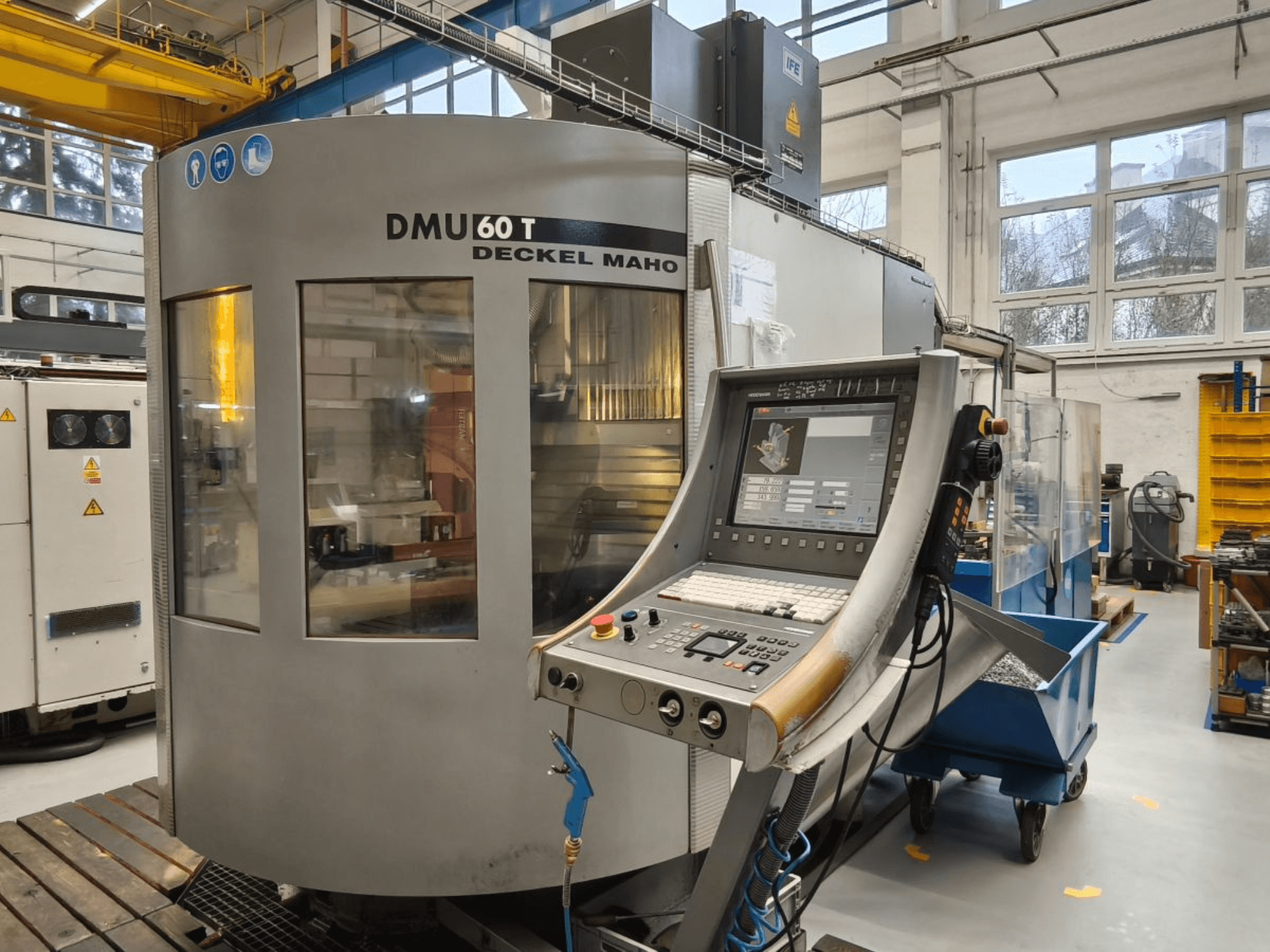 Vertikální pohled na obráběcí centrum DECKEL MAHO DMU 60T s ovládacím panelem, zobrazujícím přesné nástroje v dílně.
