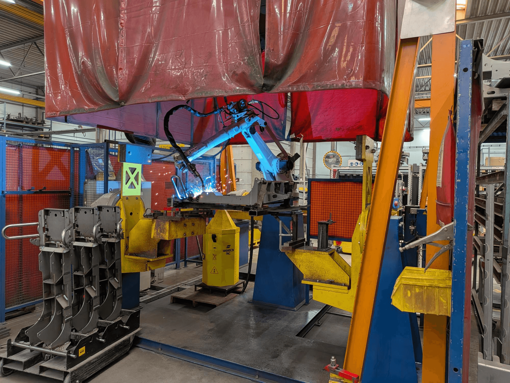 Svařovací robot OTC Daihen DR4200 v akci, pohled zepředu, s jasně modrým svařovacím obloukem a ochranným krytem.