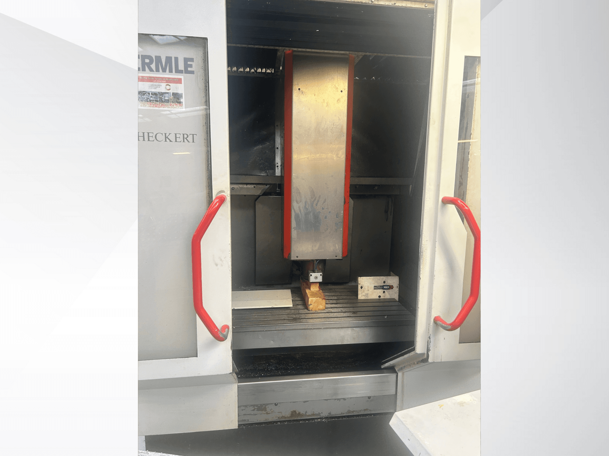 Pohled zepředu na CNC stroj Hermle s kovovým interiérem, červenými rukojeťmi a obrobkem na stole.