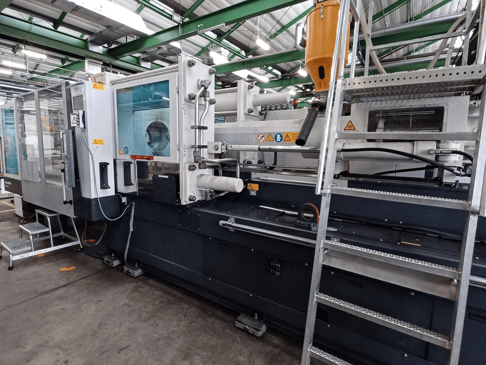 Průmyslový vstřikovací stroj s přehledným pohledem zepředu, na kterém je vidět označení značky, ovládací panel a zásobník materiálu.