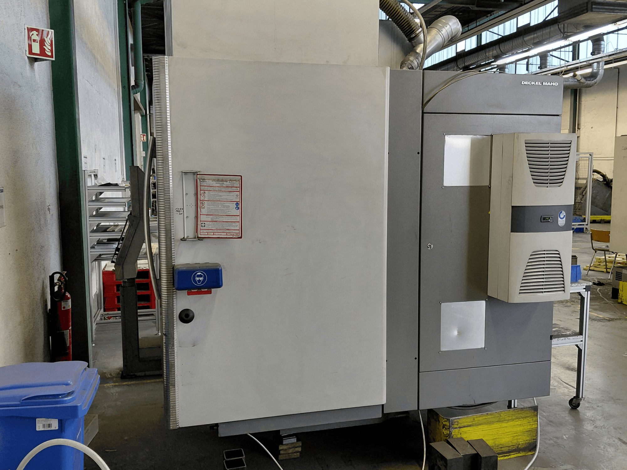 Boční pohled na vertikální obráběcí centrum DECKEL MAHO DMC 635 V s viditelným ovládacím panelem a bezpečnostními štítky.