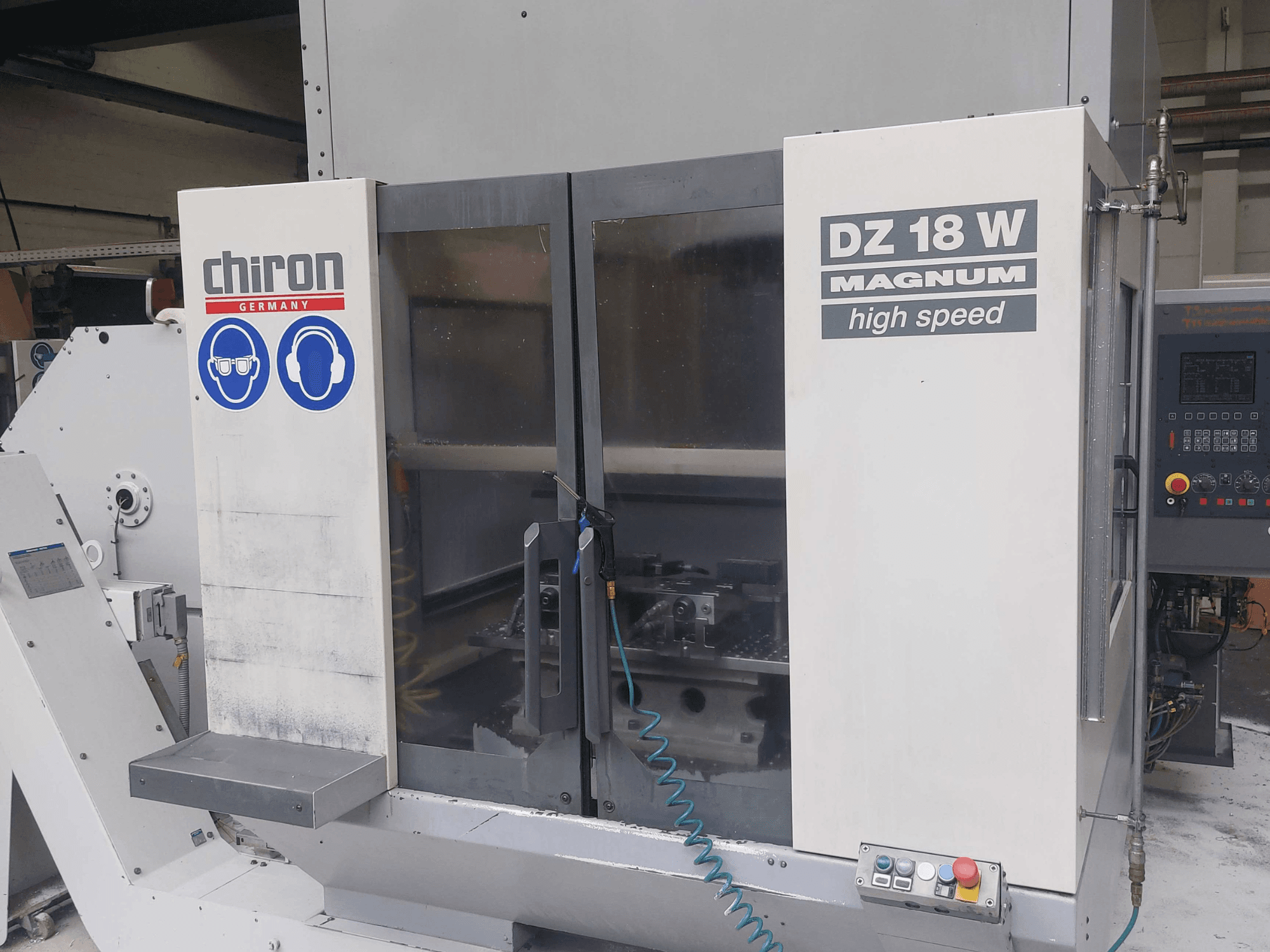 Vertikální obráběcí centrum CHIRON DZ 18 W MAGNUM, pohled zepředu s ovládacím panelem a bezpečnostními značkami.