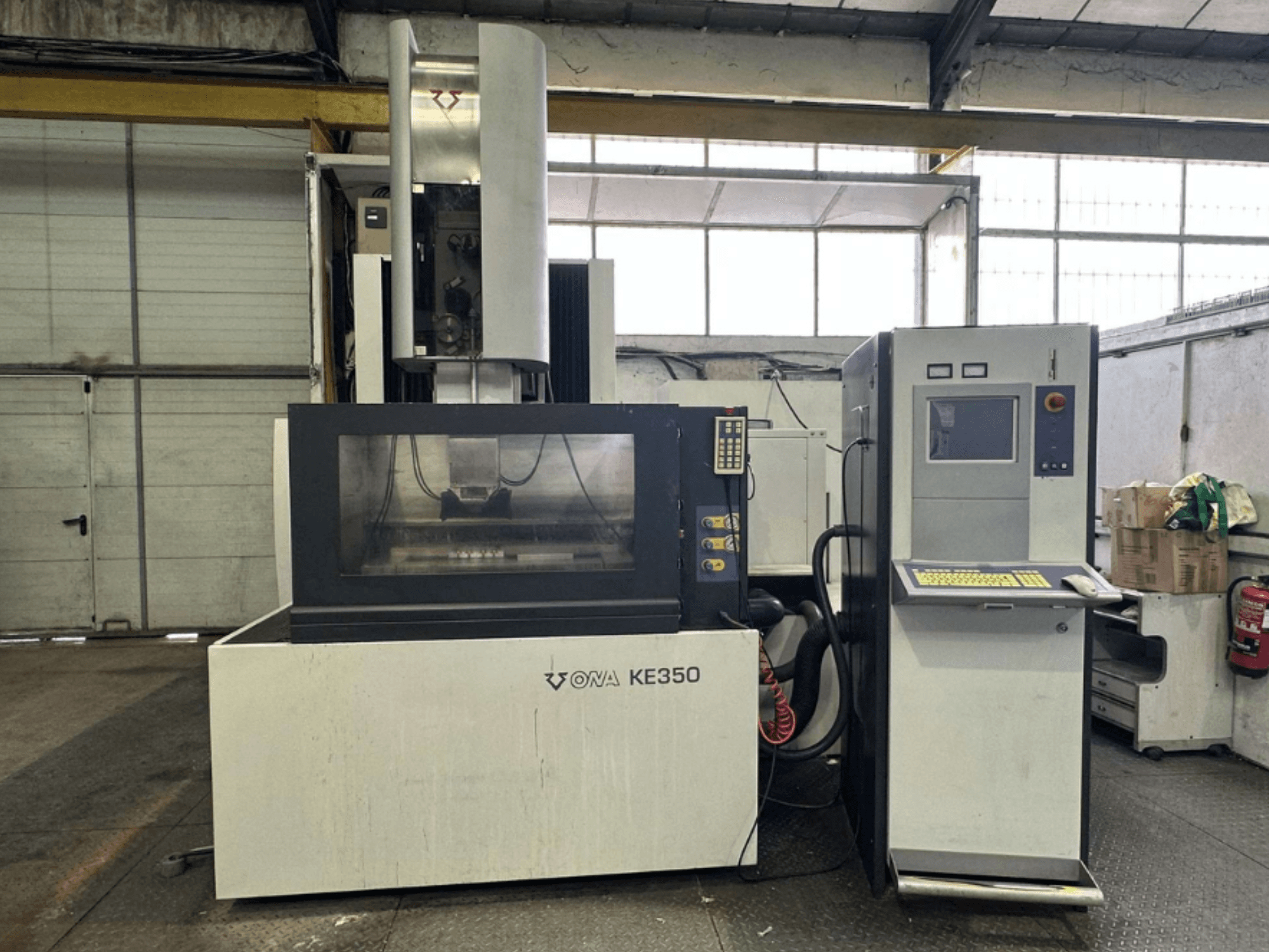 Pohled zepředu na CNC stroj ONA KE350 s ovládacím panelem, obrazovkou a různými tlačítky v průmyslovém prostředí.