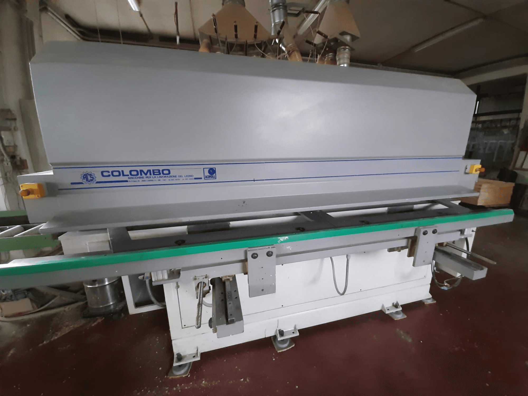 Stroj na zpracování dřeva Colombo, pohled zepředu, s dlouhým zeleným stolem, ovládacími tlačítky a šedým tělem s modrými akcenty.