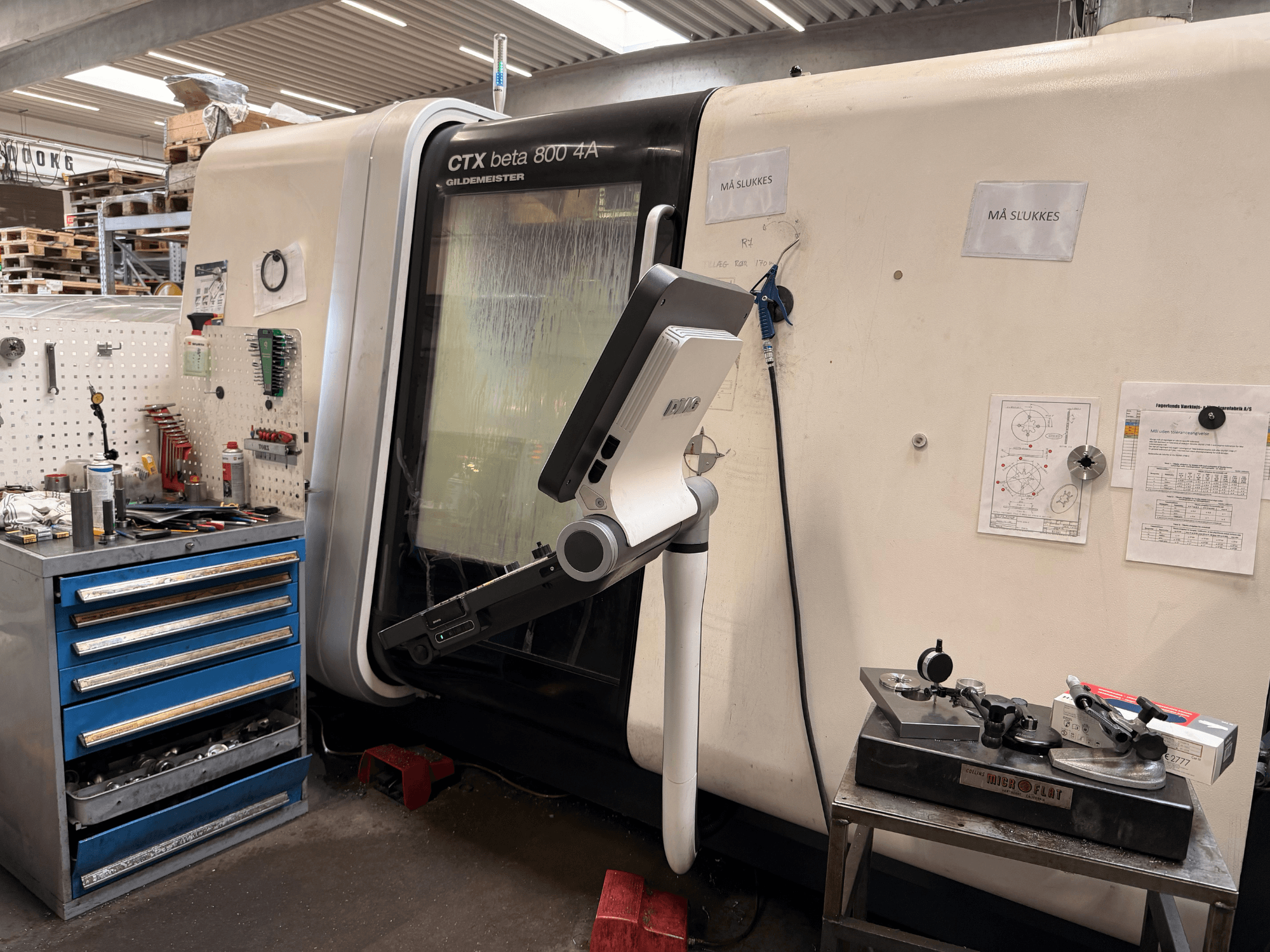 Vertikální soustruh DMG MORI CTX Beta 800 4a v dílně, s řídicím ramenem a technickou dokumentací v blízkosti.