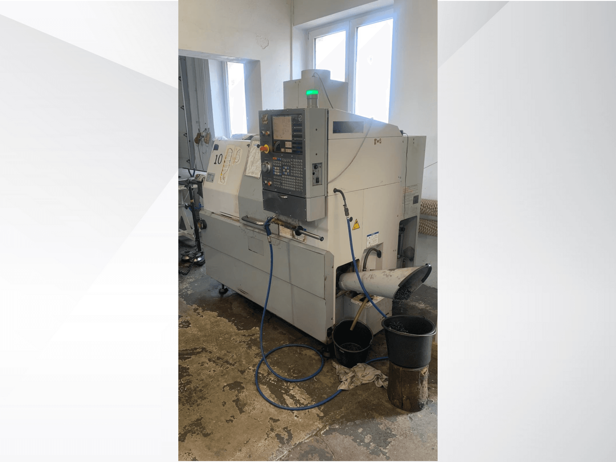 Model CNC stroje Haas s ovládacím panelem, boční pohled, s chladicím potrubím, odpadním žlabem a úložnými nádobami pod ním.