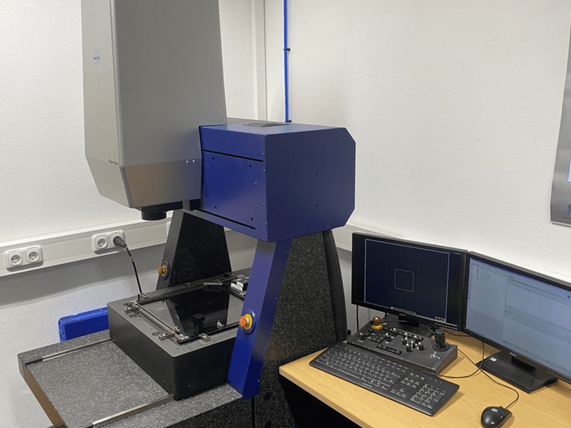 Souřadnicový měřicí stroj Werth Scope-Check 400 v laboratoři, zobrazující měřicí hlavu a ovládací panel s obrazovkami a klávesnicí.