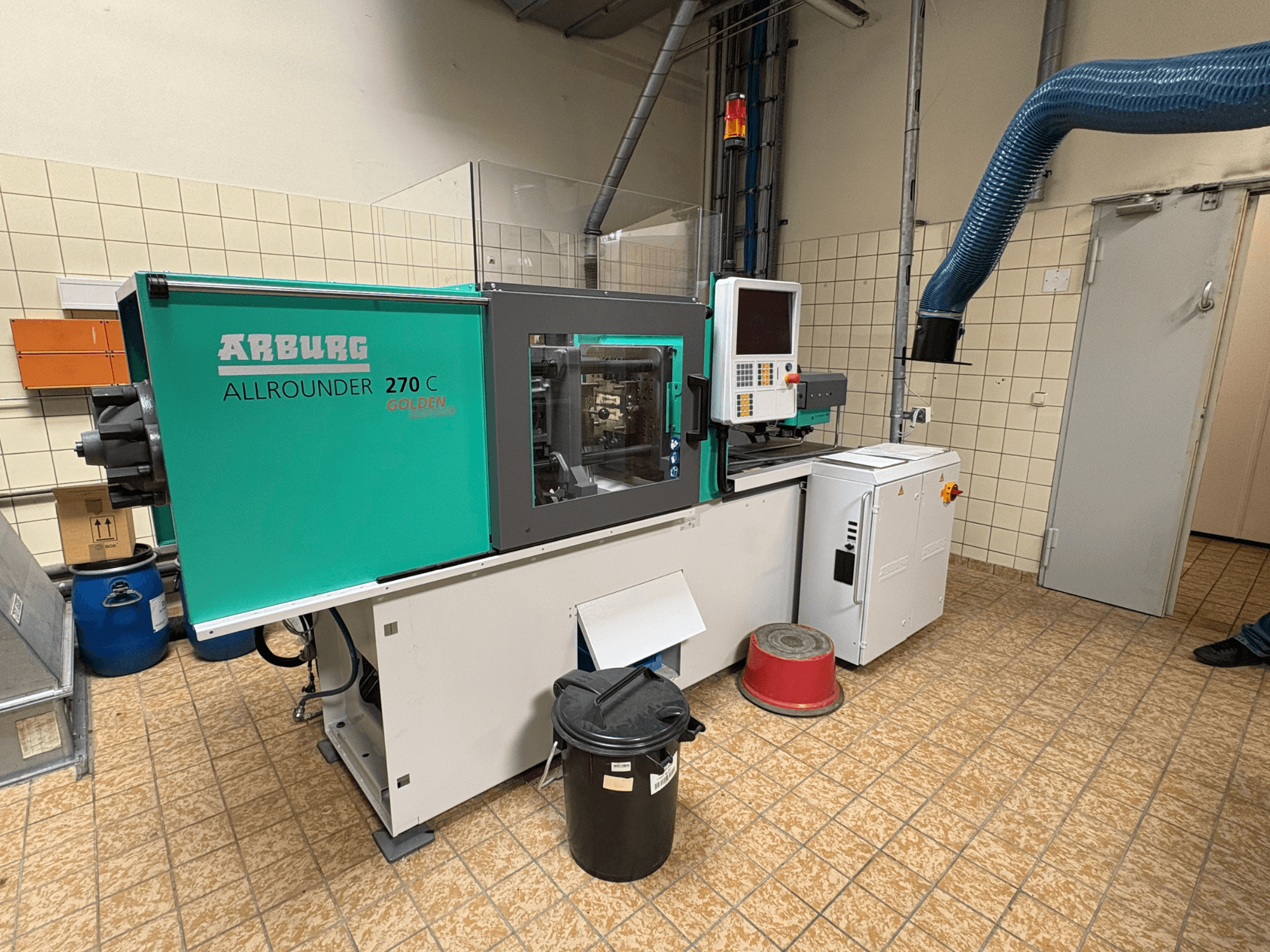 Hydraulický vstřikovací lis Arburg ALLROUNDER 270 C z bočního pohledu, včetně ovládacích prvků a připojeného zařízení.