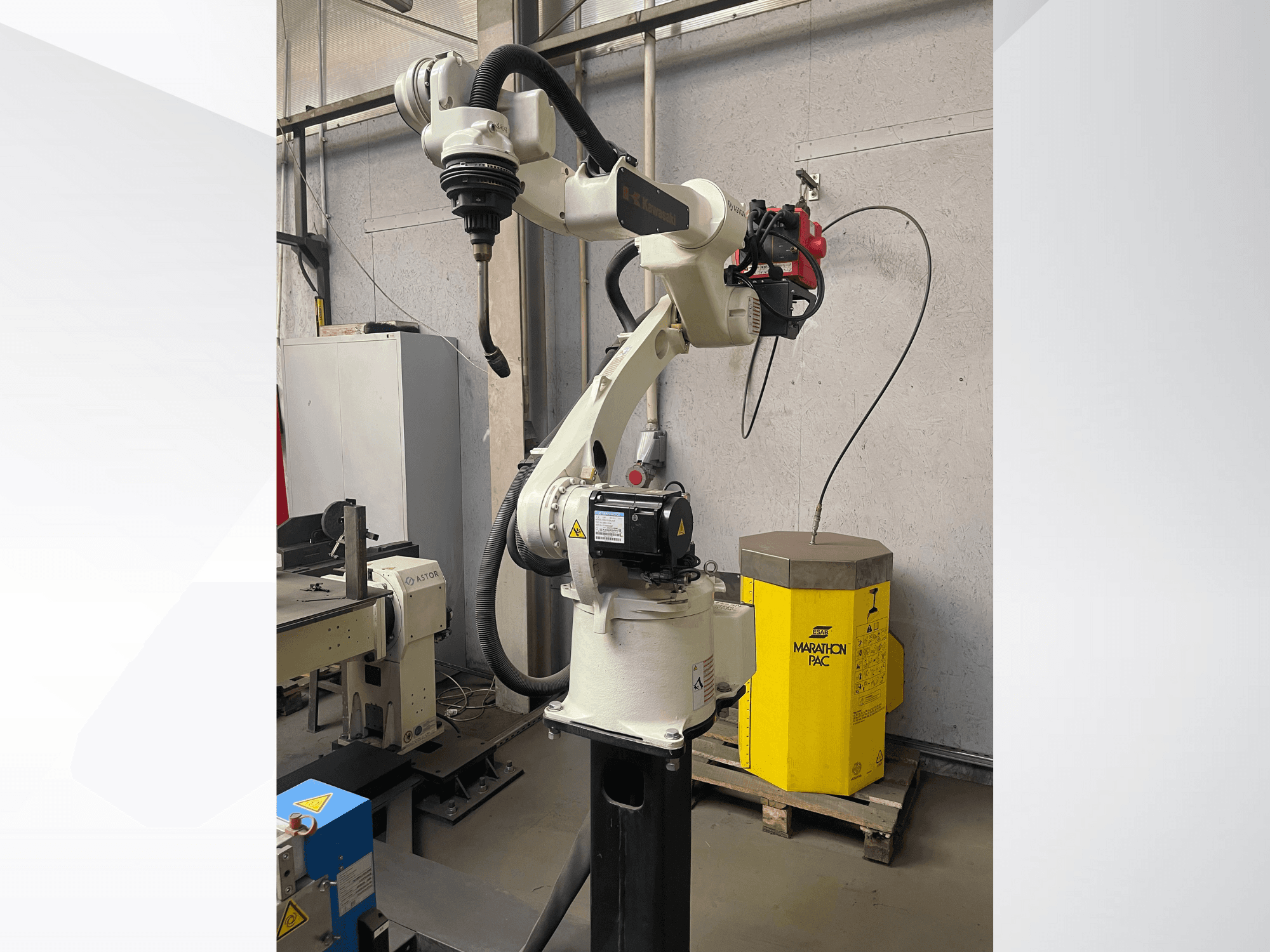 Robotické rameno Kawasaki z bočního pohledu s namontovaným držákem nástrojů a žlutou pohonnou jednotkou v pozadí.