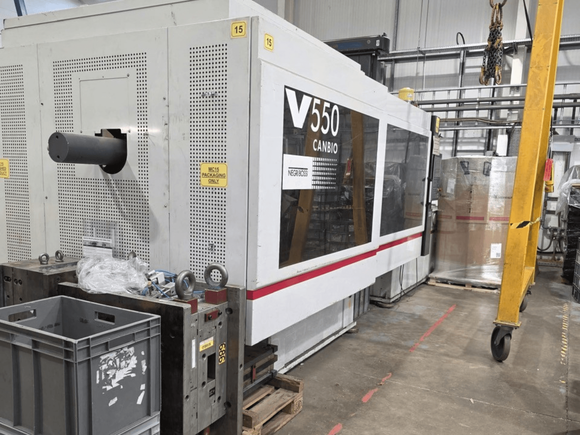 Hydraulický vstřikovací stroj Negri Bossi V55000H-4250, boční pohled, s ovládacím panelem a šedými bednami v popředí.