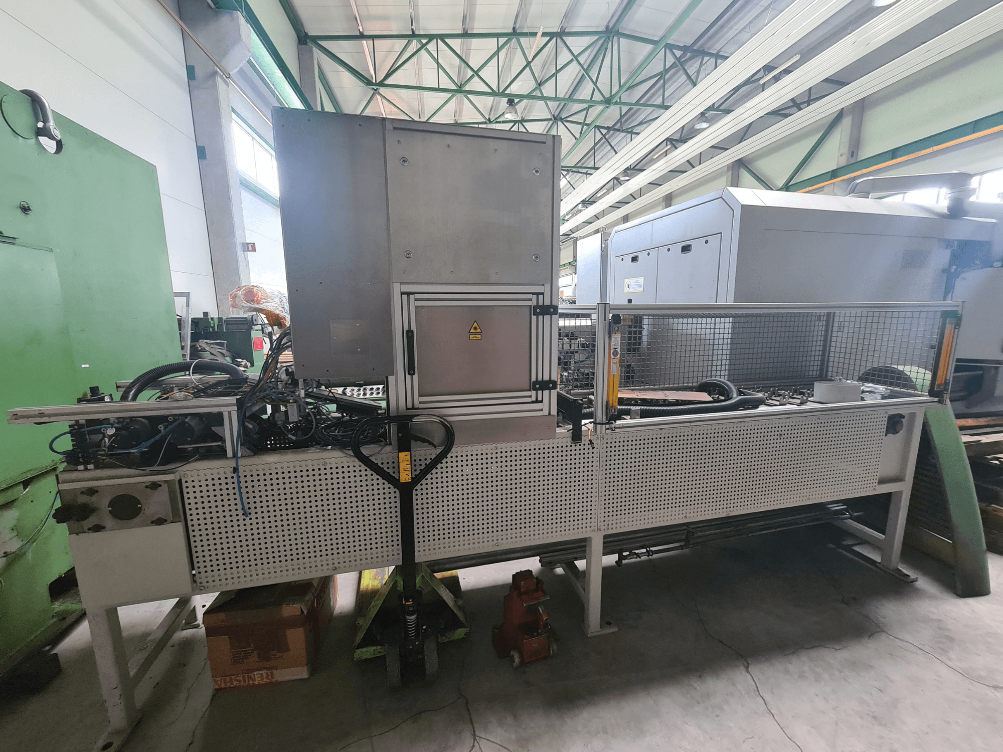 Průmyslové stroje s kovovým rámem, hadicemi a ovládacím panelem, pohled z boku v továrním prostředí.