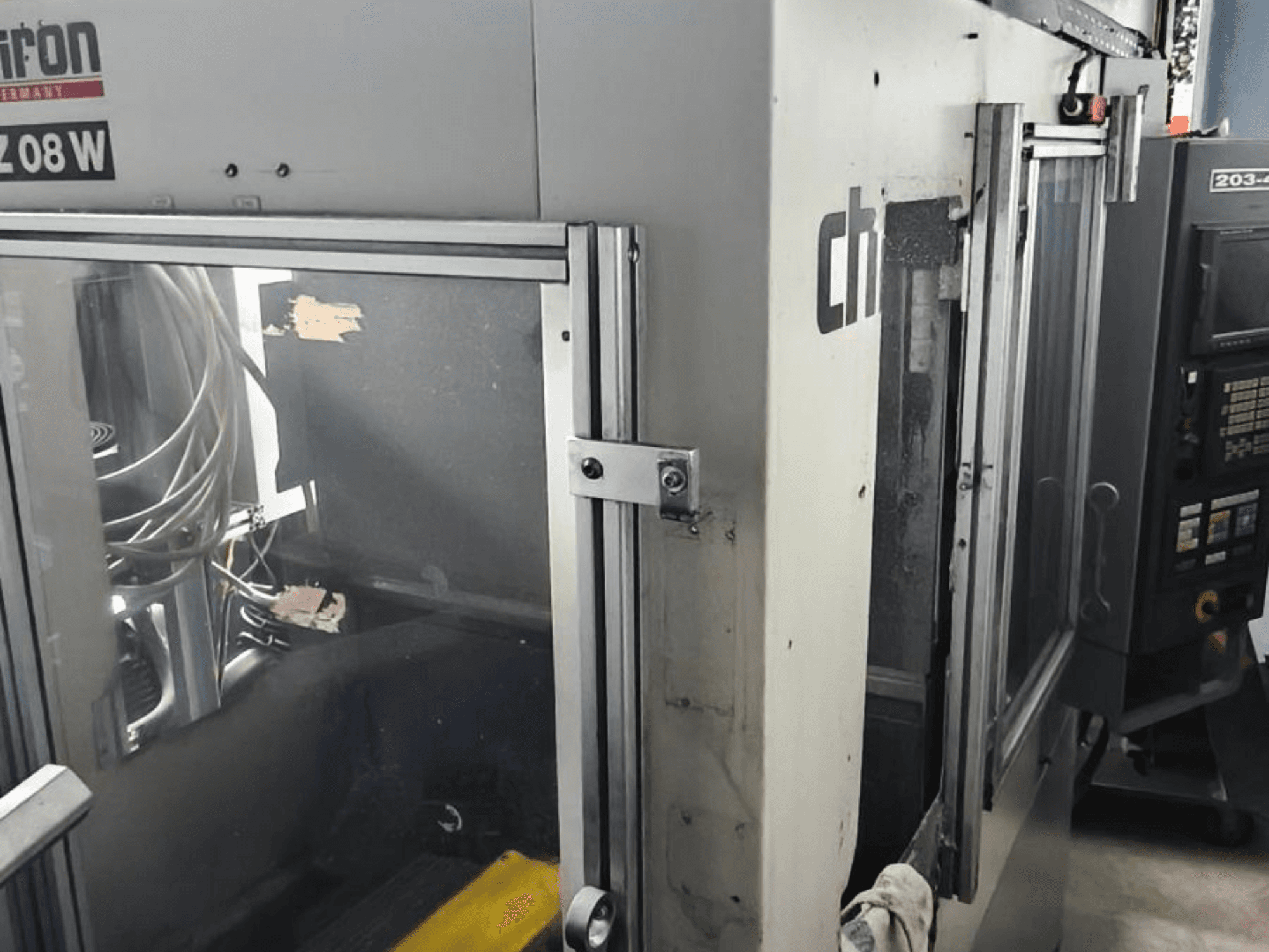 Vertikální obráběcí centrum CHIRON FZ 08 W, pohled zepředu na ovládací panel a částečně otevřené dveře, s viditelnými vnitřními součástmi.