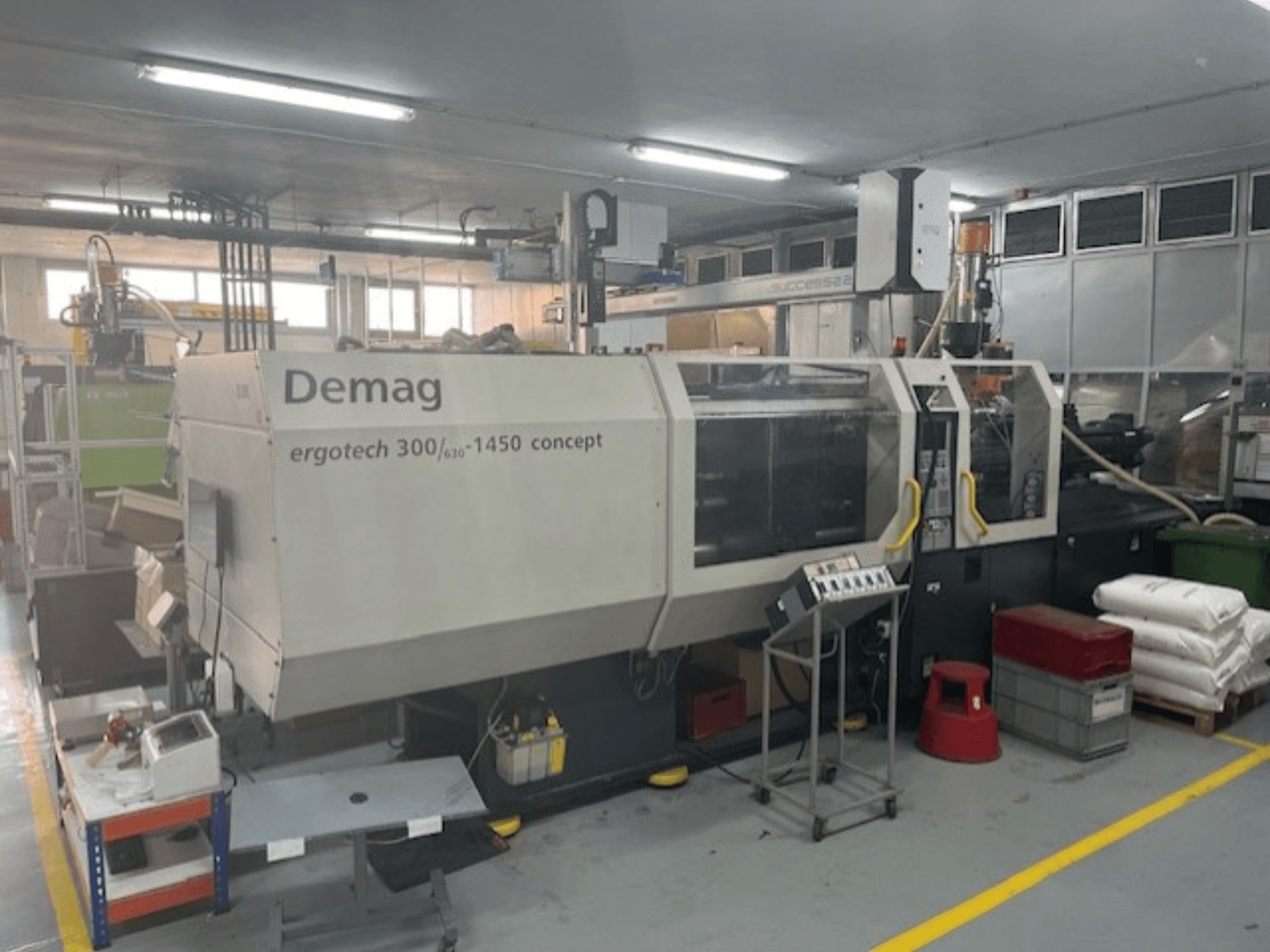 Hydraulický vstřikovací stroj Demag ERGOTECH CONCEPT 3000-1450, pohled zepředu, s ovládacími prvky a materiály v blízkosti.