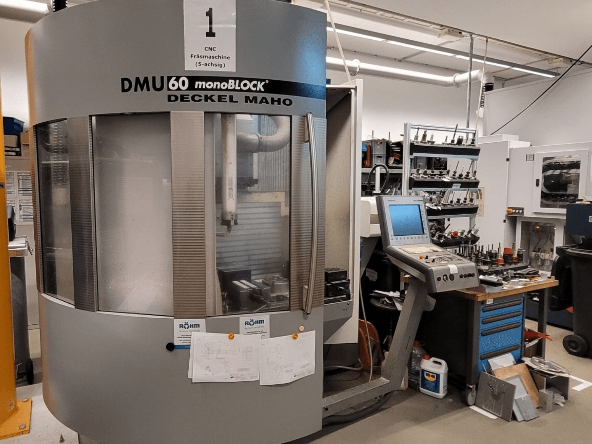CNC frézka DECKEL MAHO DMU 60 monoBLOCK v čelním pohledu, vedle ní ovládací panel a zásobník nástrojů.