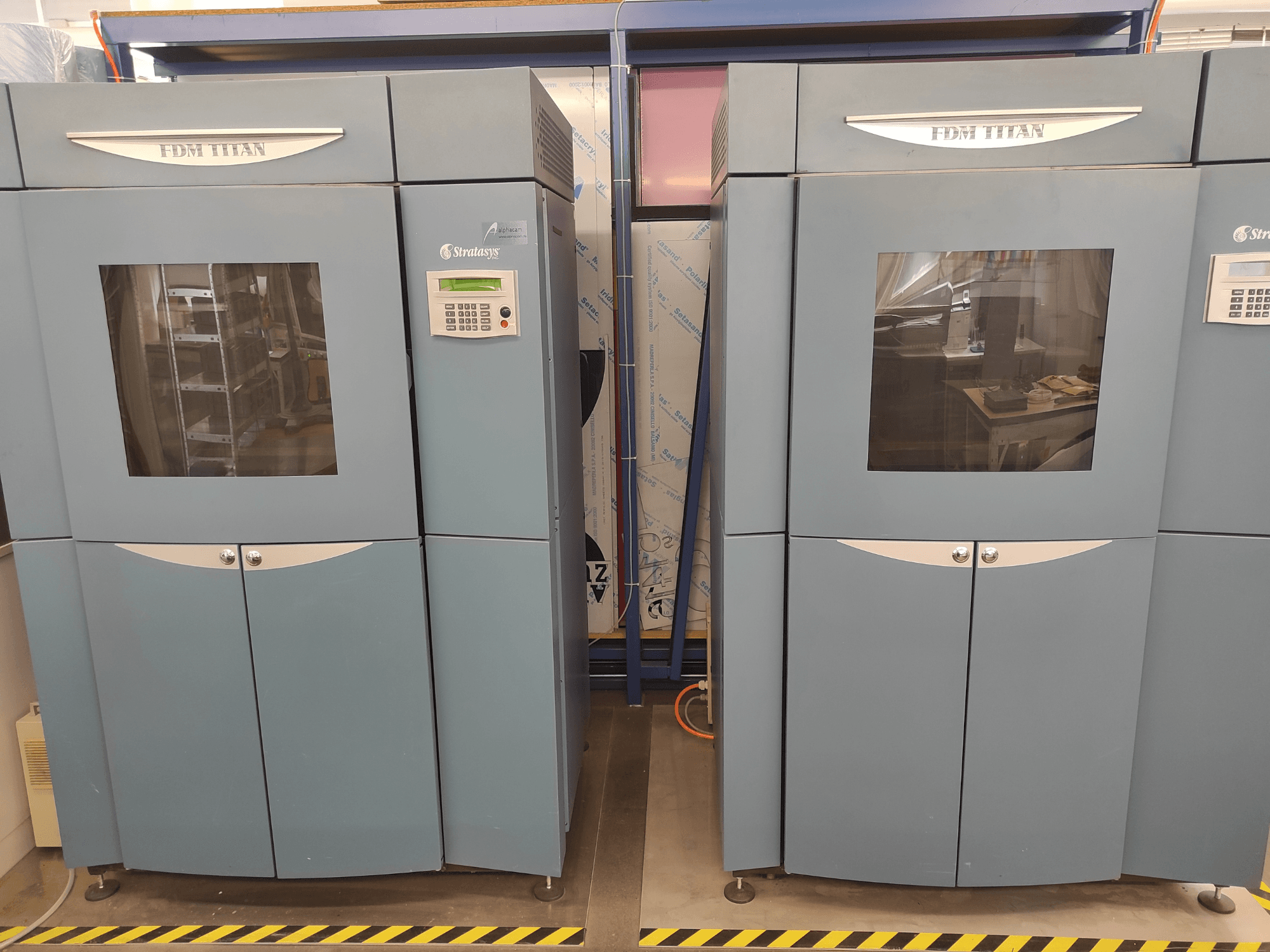 3D tiskárna FDM TitanTI od společnosti Stratasys, pohled zepředu, s dvojitými dvířky a ovládacím panelem, umístěná v průmyslovém prostředí.