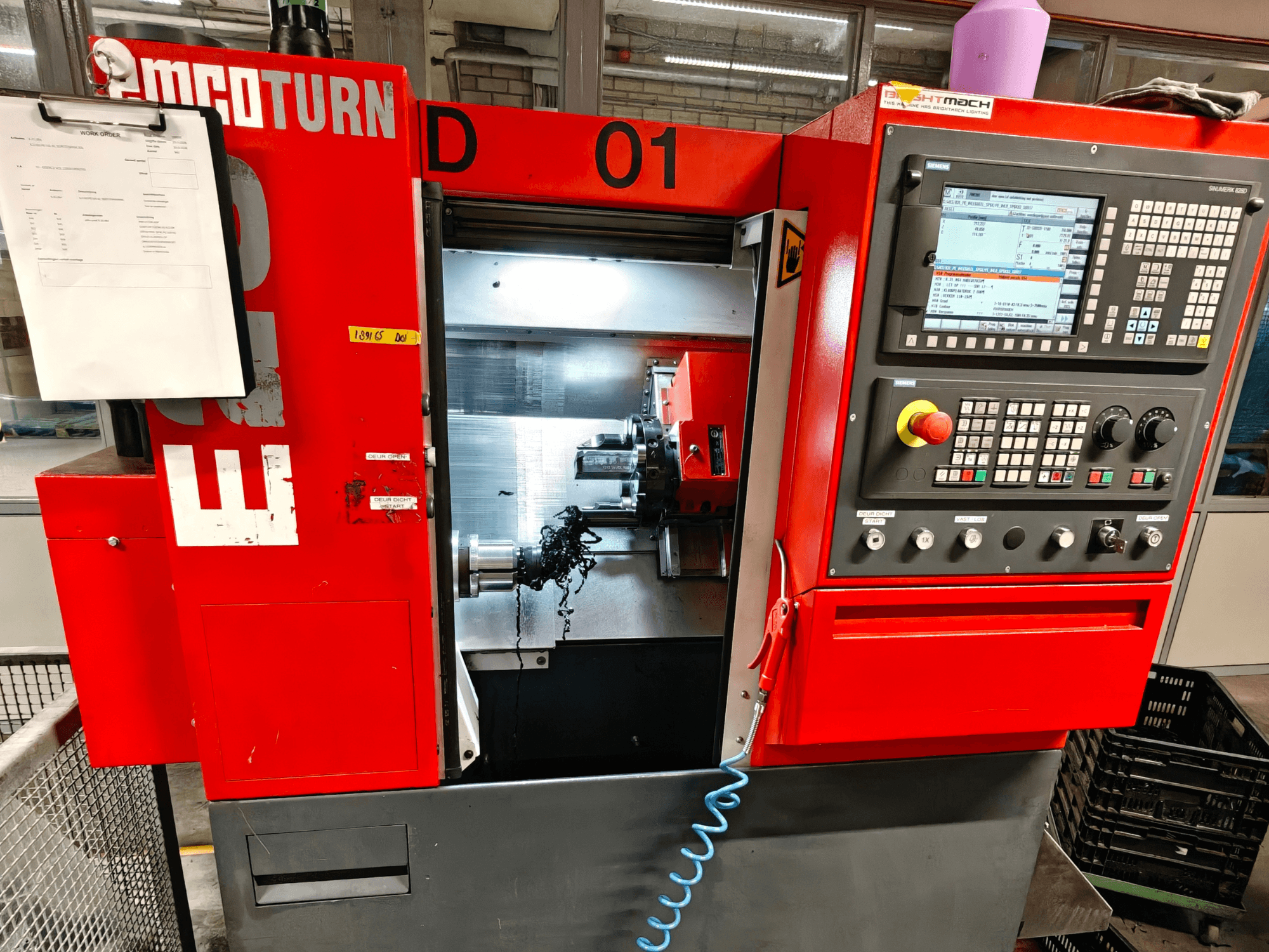 Pohled zepředu na horizontální soustruh EMCO TURN E25 s ovládacími prvky, držákem nástrojů a pracovním prostorem s třískami.