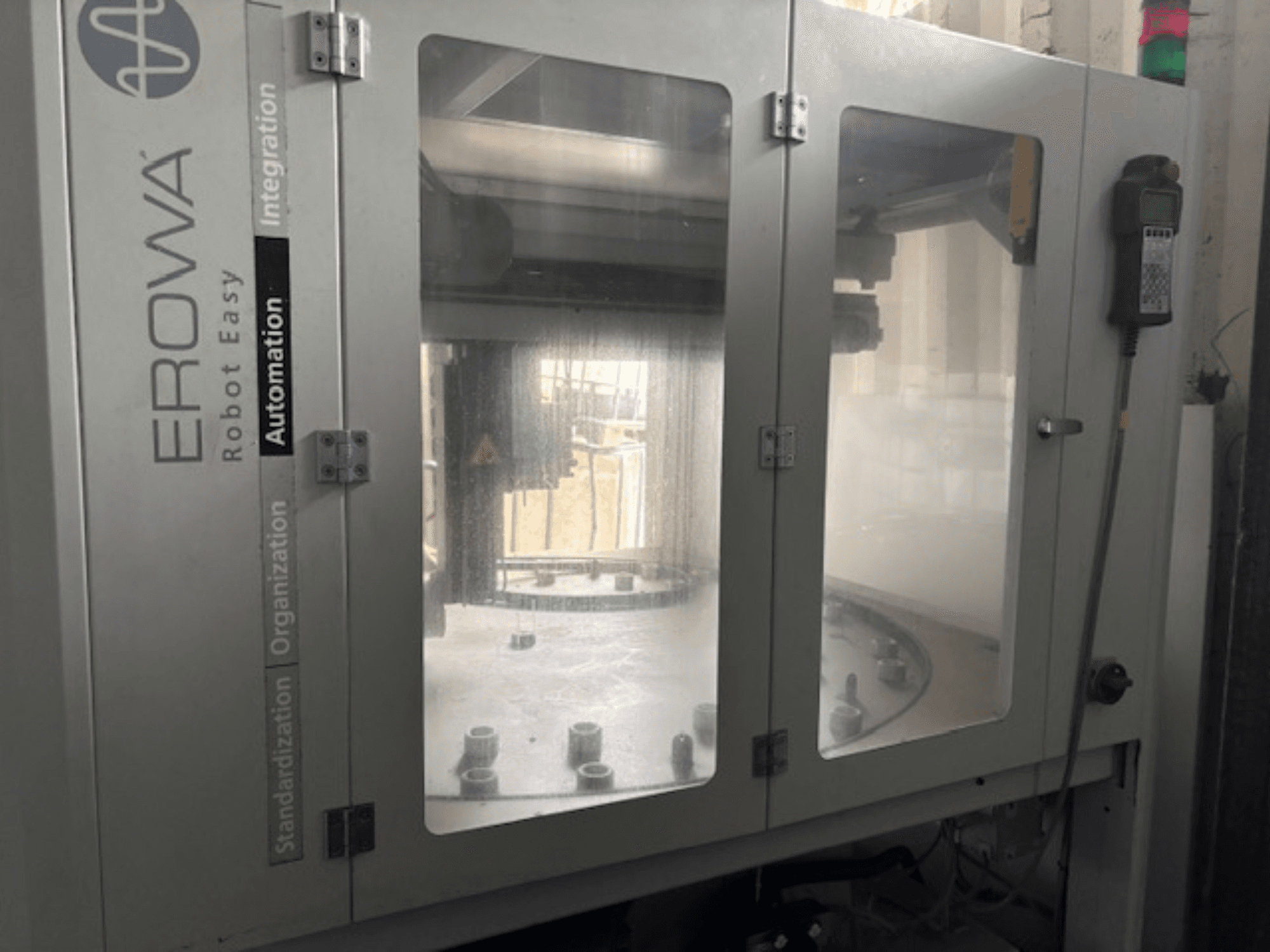 Pohled zepředu na robot EROWA Robot Easy Automation; průhledné dveře, viditelné automatizační komponenty a ovládací panel.
