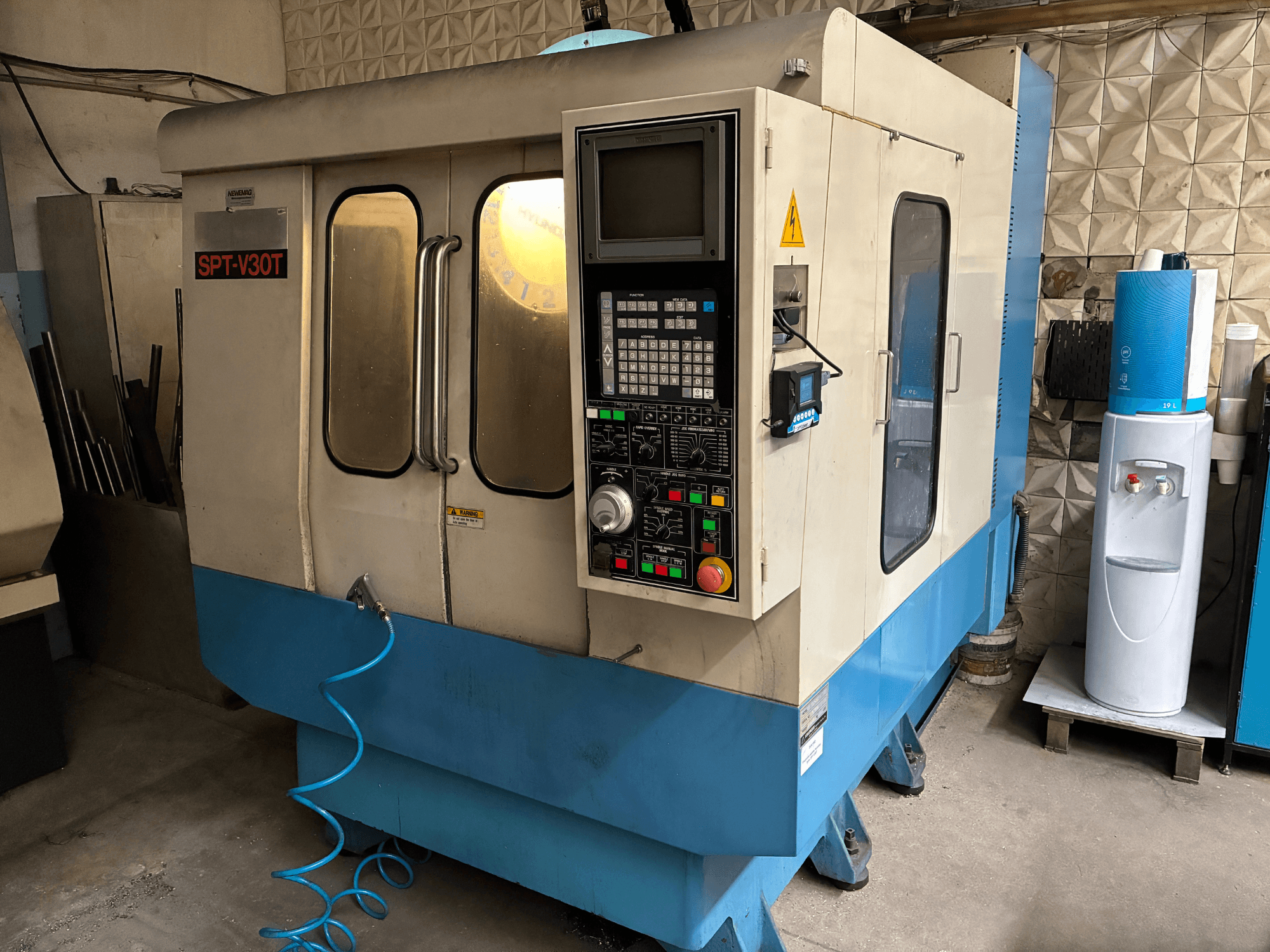 Stroj SPT-V30T CNC v modrobílém provedení, pohled zepředu ukazuje ovládací panel, dvířka a vzduchovou hadici. Ideální pro přesné obrábění.