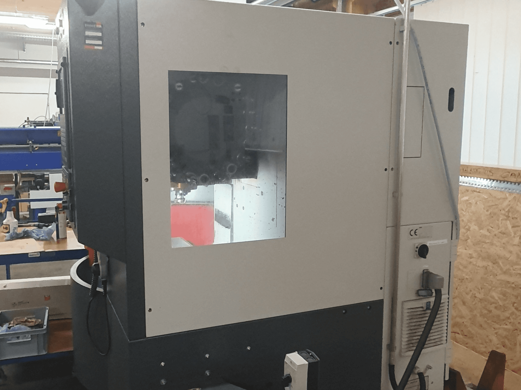 Boční pohled na obráběcí stroj s viditelným ovládacím panelem, velkým průzorem a složitými vnitřními součástmi.