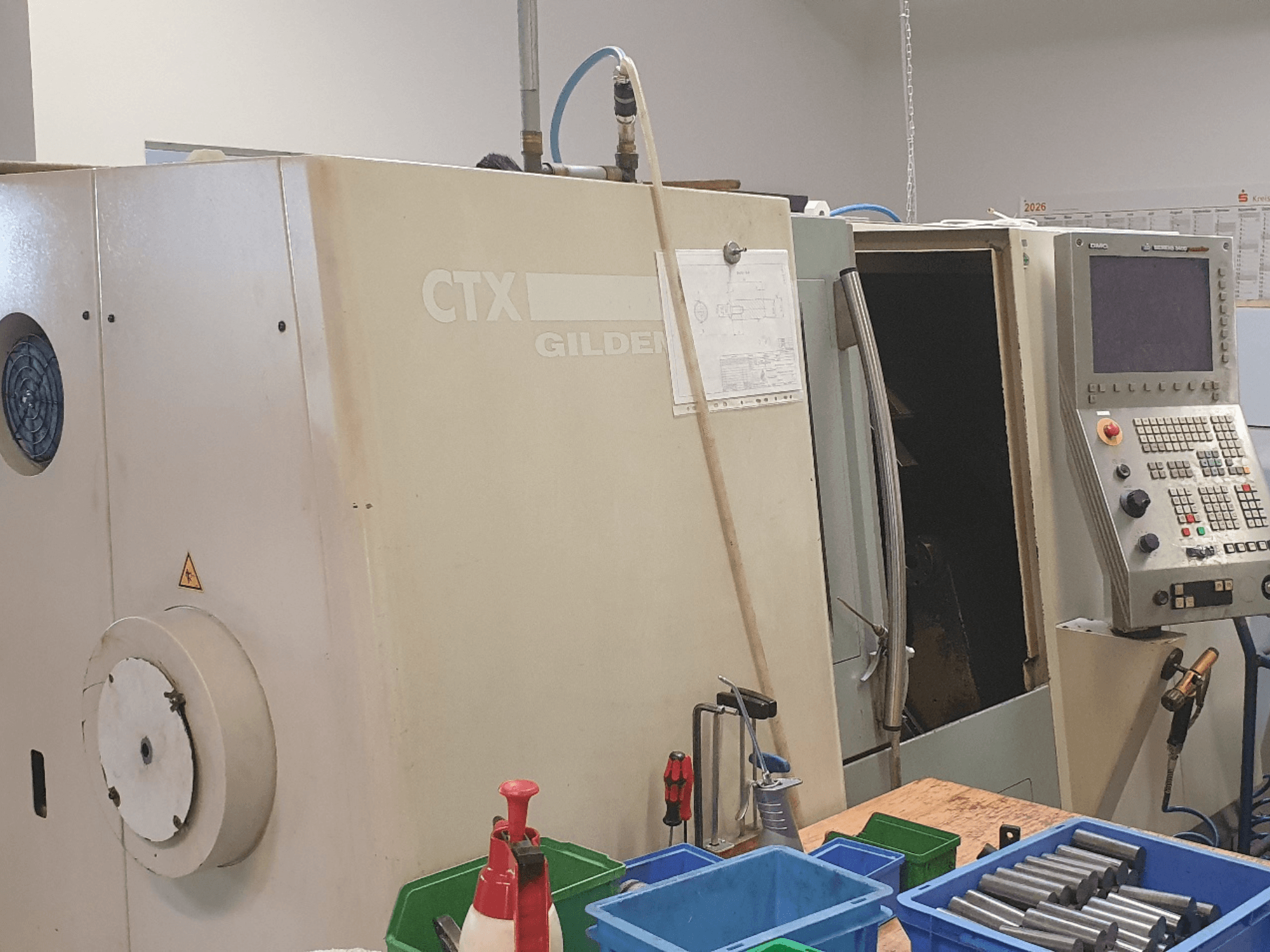 Pohled zepředu na horizontální soustruh DMG GILDEMEISTER CTX 310, viditelný ovládací panel, v popředí nástroje a nádoby.