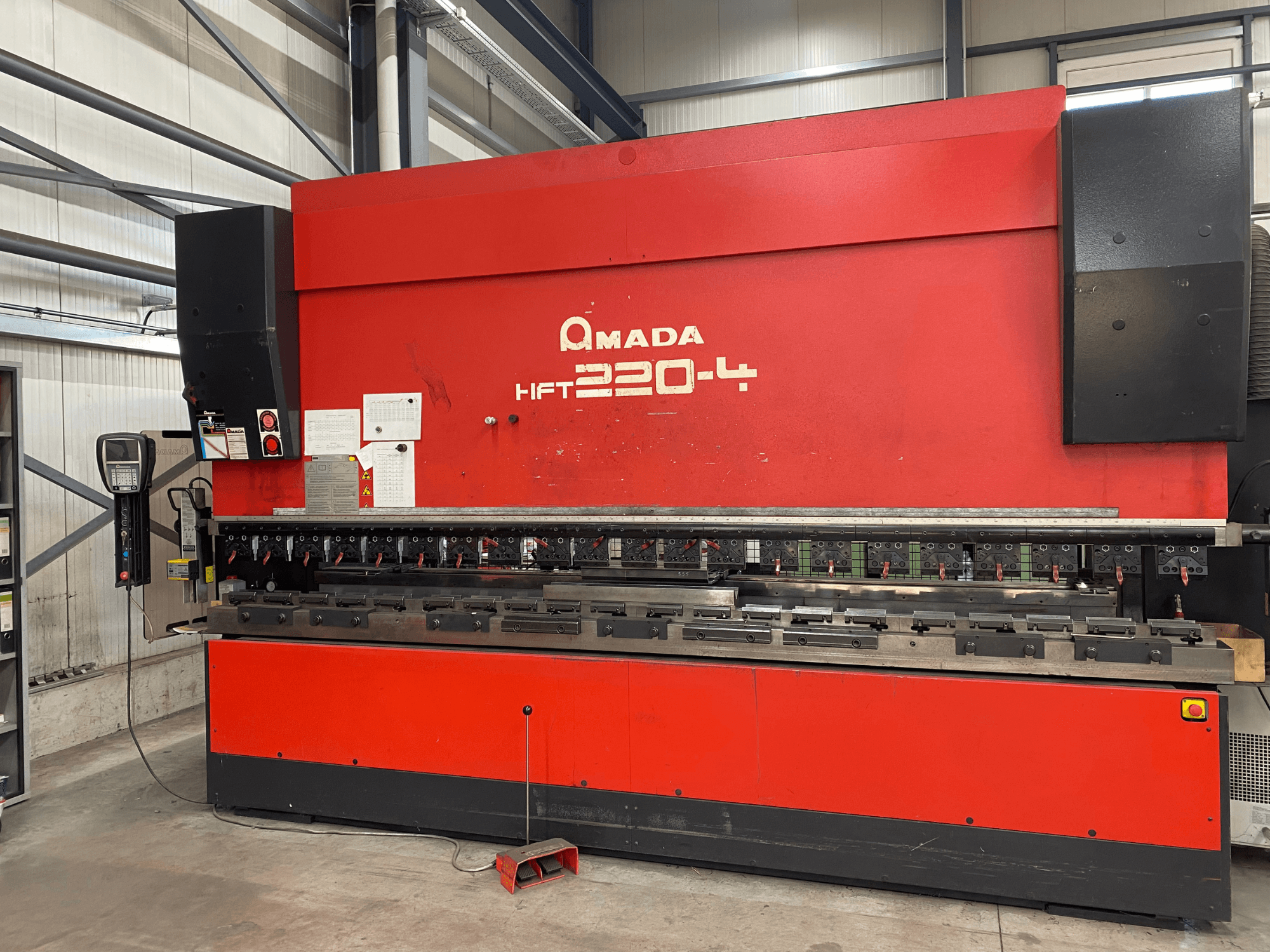 Červená ohraňovací stolice AMADA HFT 220-4 v továrním nastavení, pohled zepředu ukazuje ovládací panel a ohýbací nástroje na pracovní ploše.