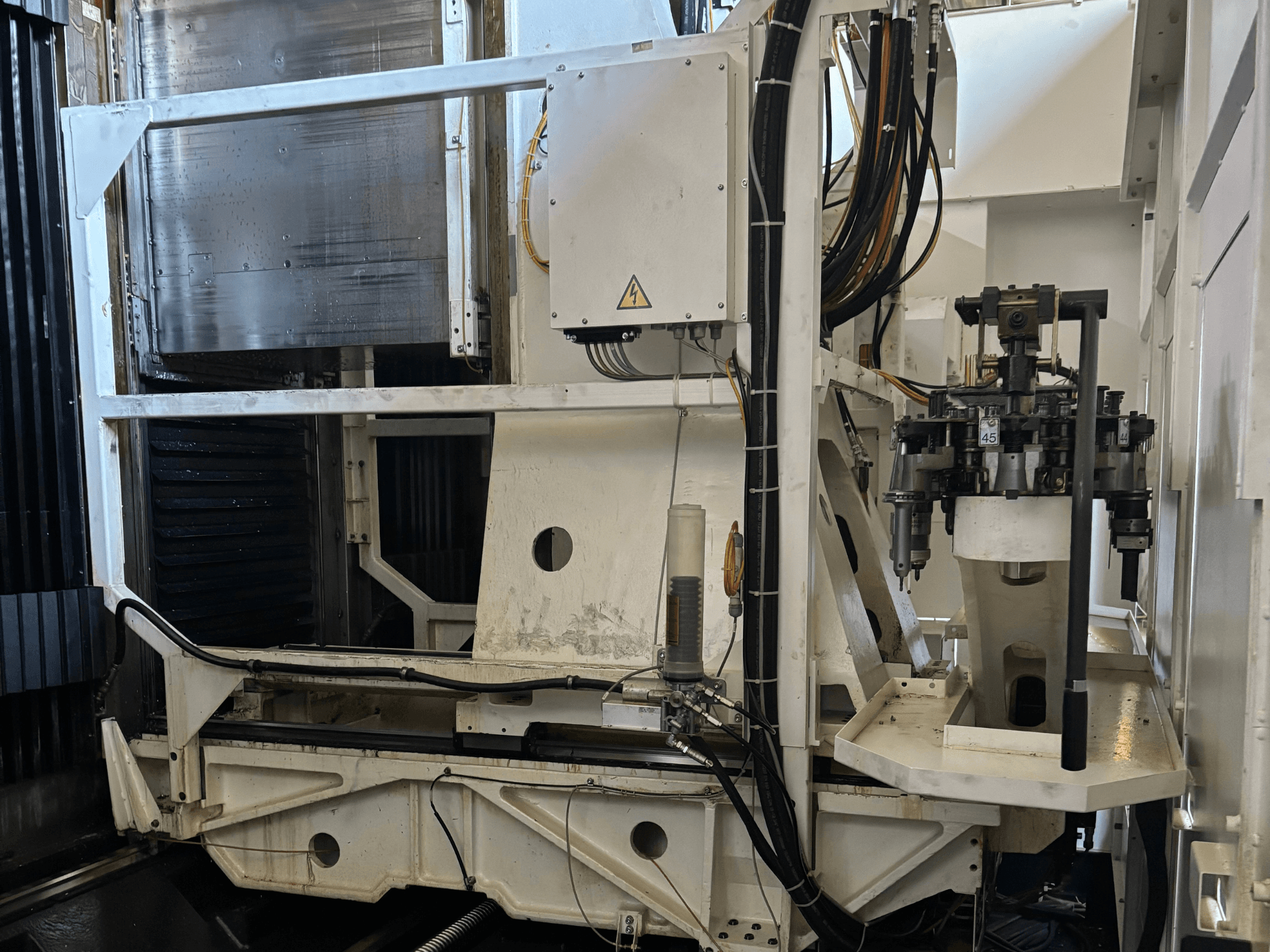 Boční pohled na průmyslový stroj zobrazující bílou CNC frézku s viditelnými nástroji, trubkami a ovládacím panelem.