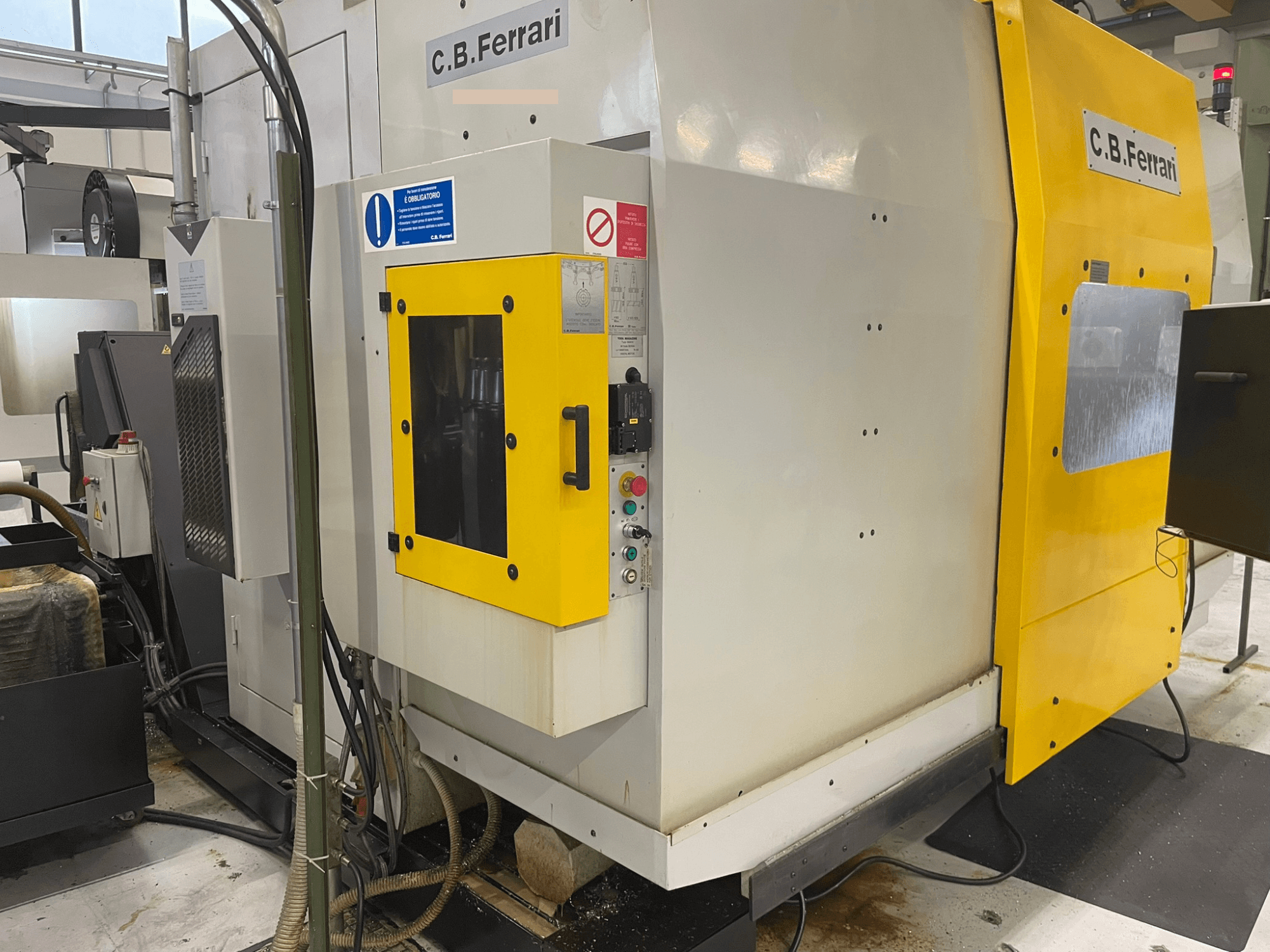 Průmyslový stroj C.B. Ferrari, pohled zepředu; žlutá dvířka, ovládací panel a viditelné obráběcí součásti.