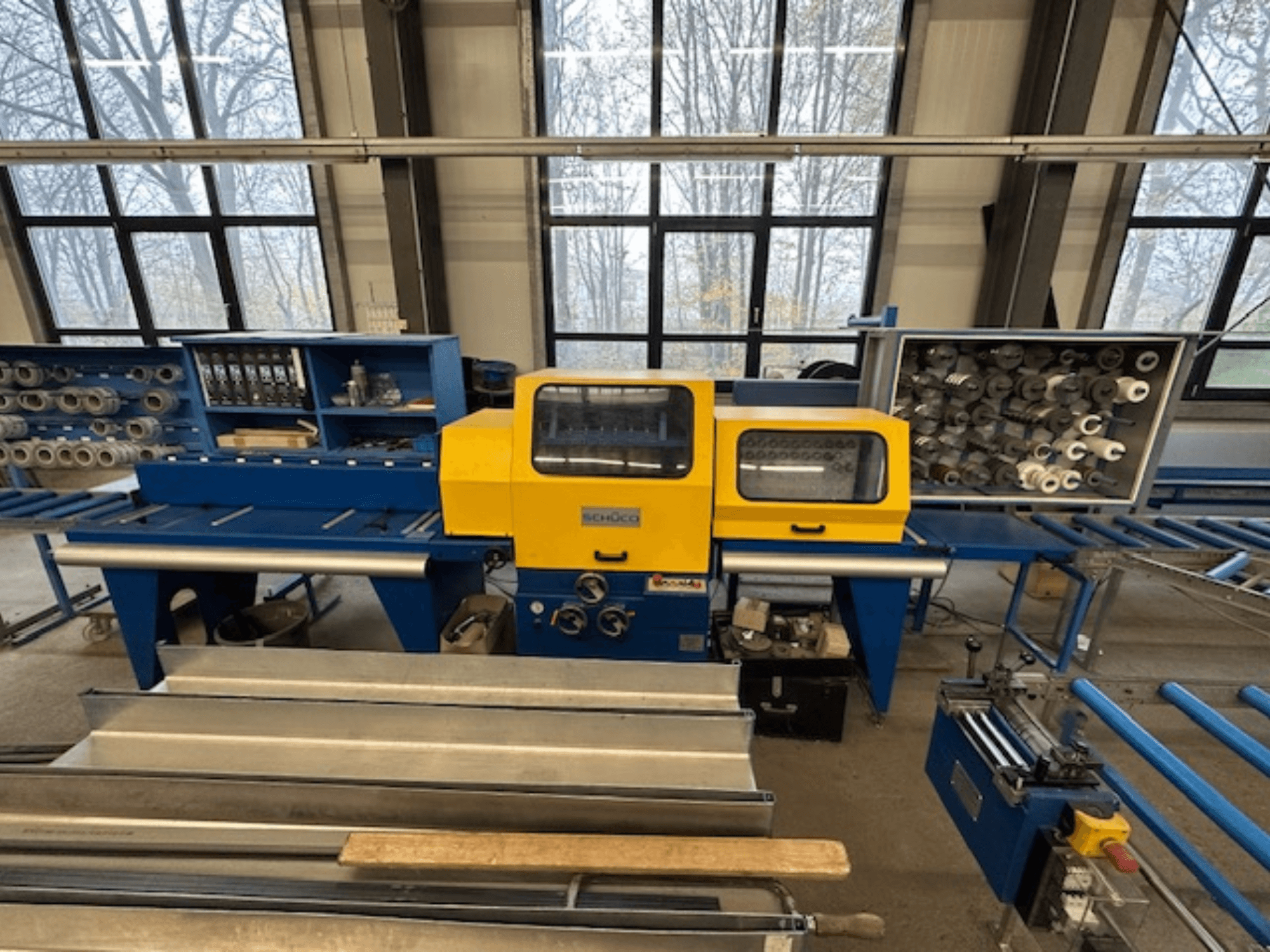 Pohled zepředu na obráběcí stroj SCHÜCO ISOMAT 4 se žlutým ovládacím panelem, několika válci a úložným prostorem.