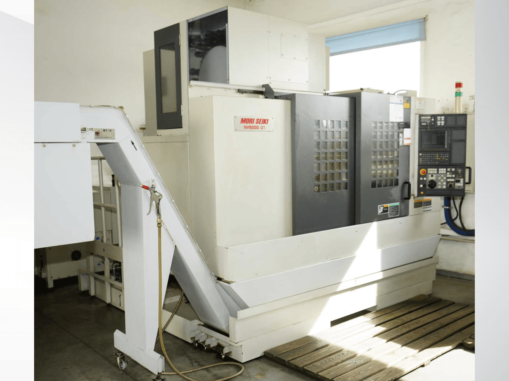 Vertikální obráběcí centrum MORI SEIKI NV 5000 alpha1 v čelním pohledu, na kterém je vidět ovládací panel, bezpečnostní prvky a nakládací prostor.