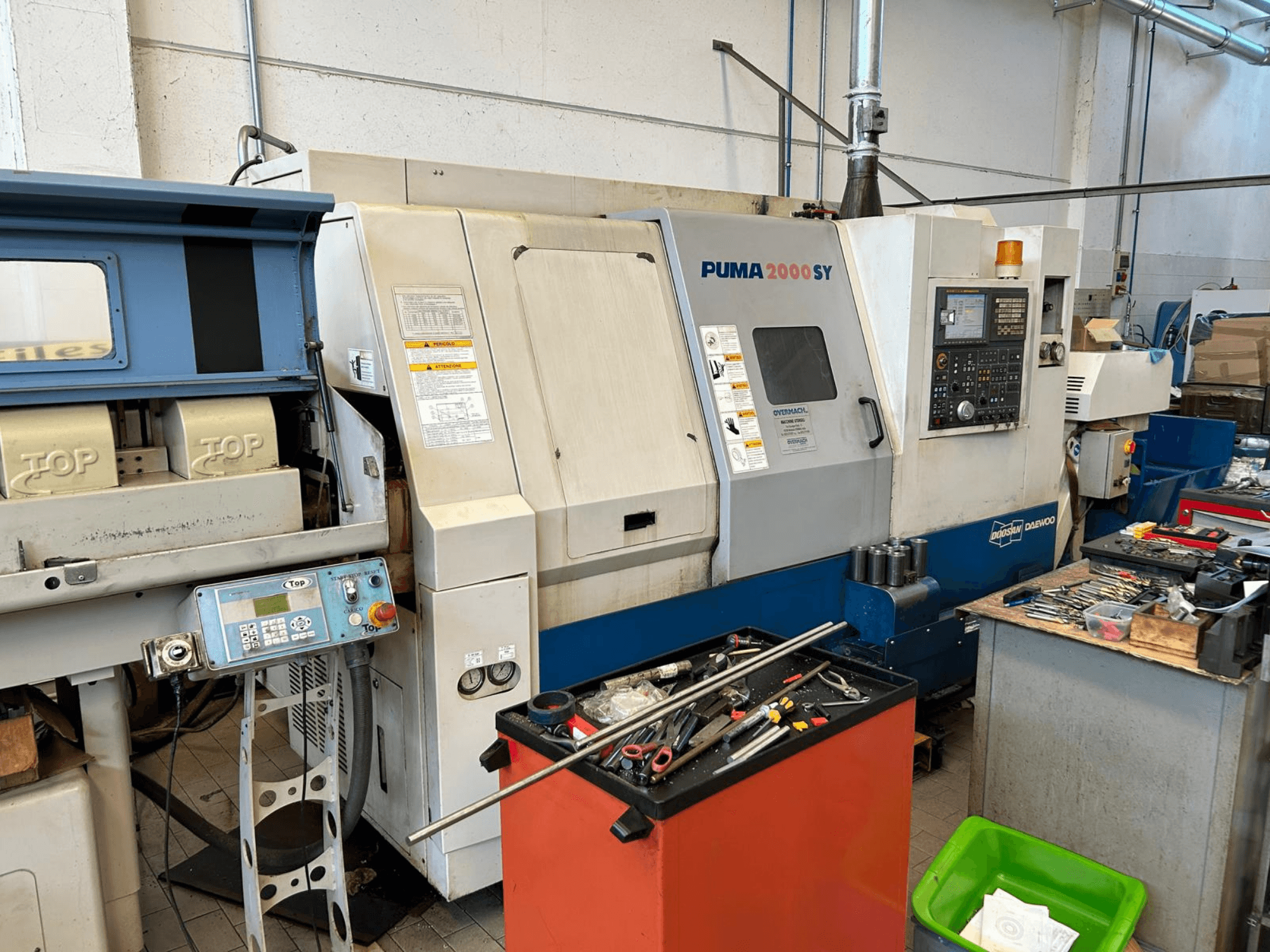 Horizontální soustruh DOOSAN PUMA 2000SY v dílně, boční pohled znázorňující ovládací panel a nástroje v jeho blízkosti.