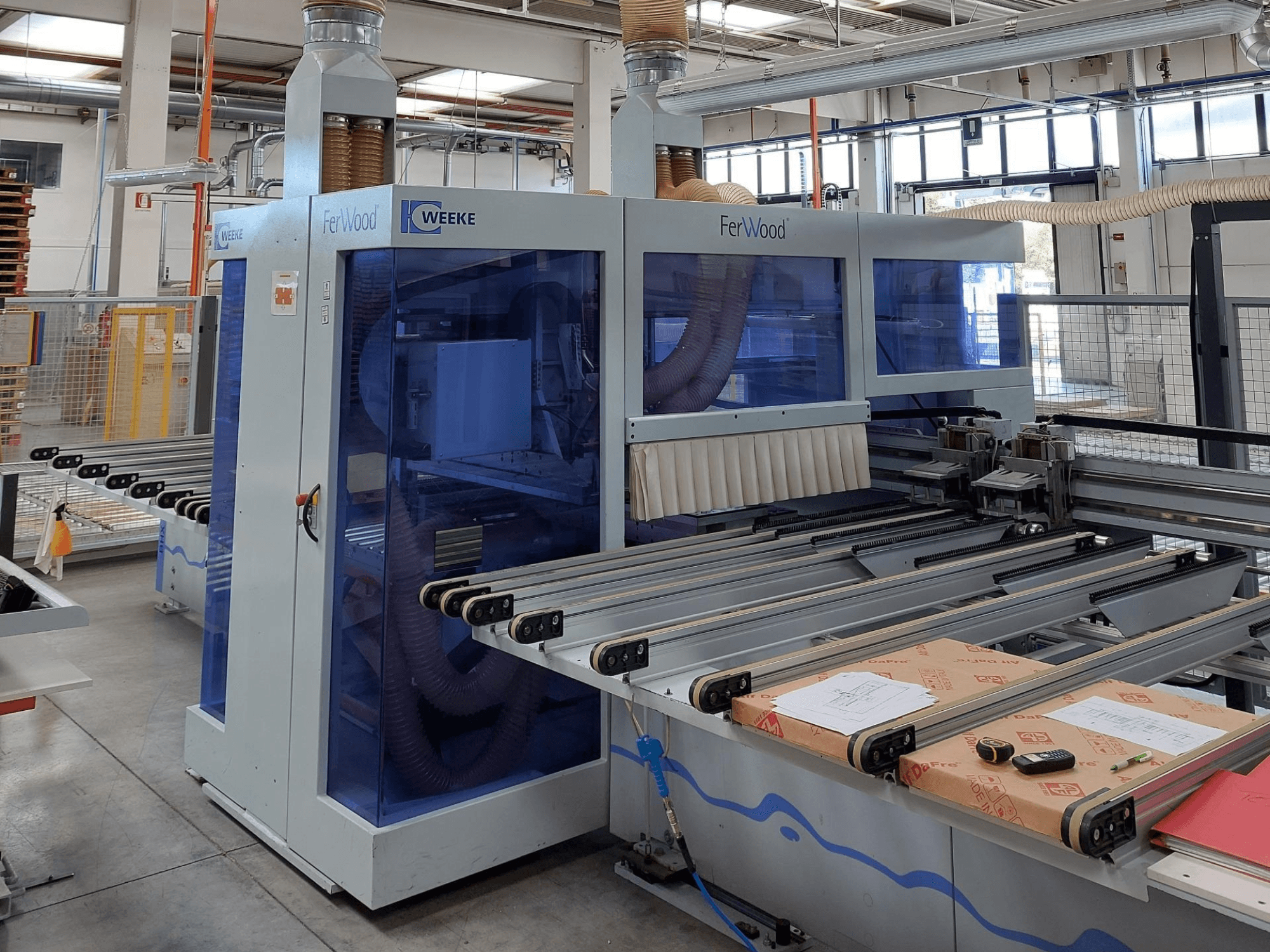 CNC stroj Weeke FerWood v dílně, pohled zepředu ukazuje modře podbarvené panely, ovládací tlačítka a pracovní stůl s materiály.