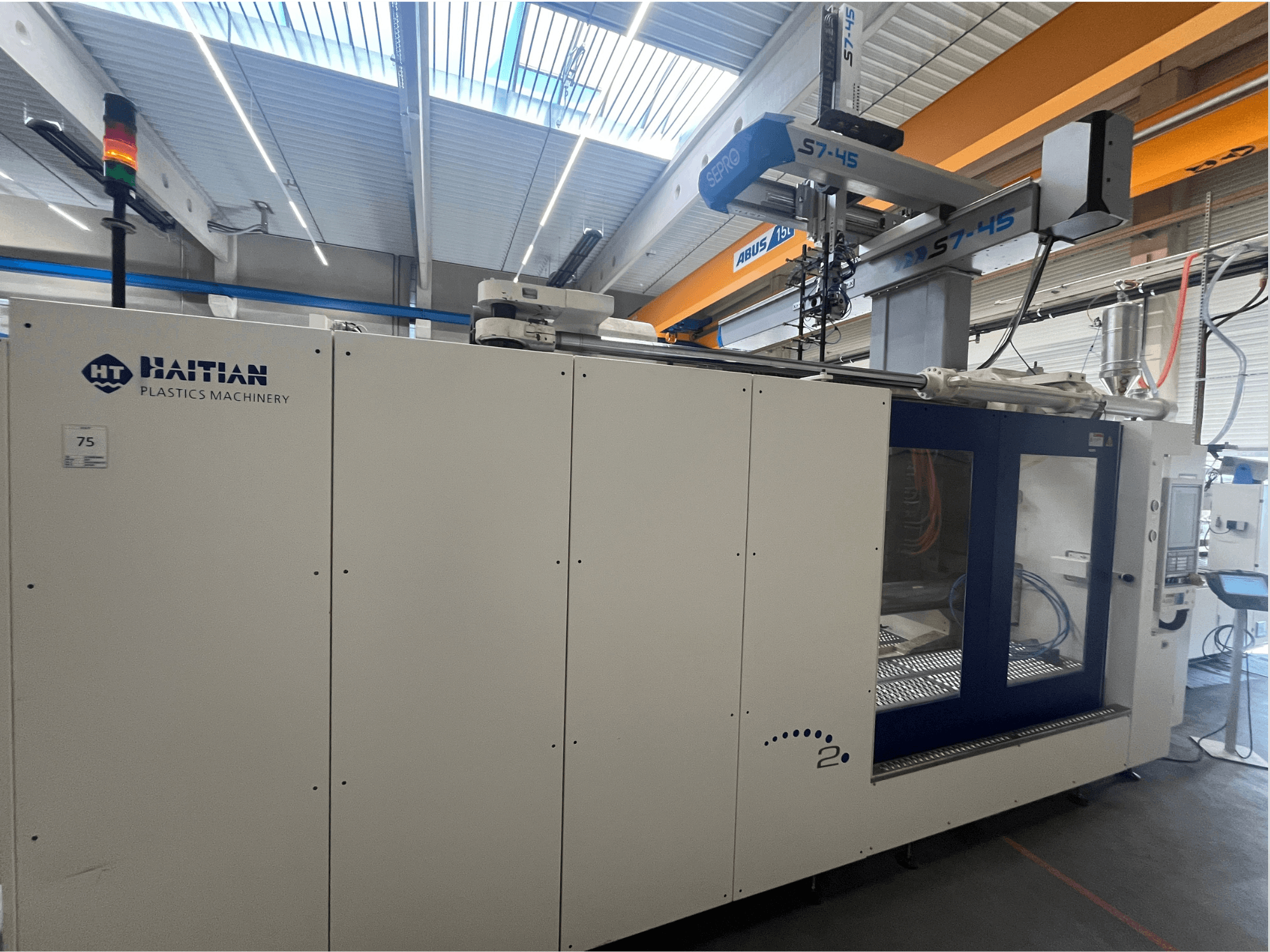 Vstřikovací stroj Haitian S7-45 v bočním pohledu s ovládacím panelem a bezpečnostním světelným indikátorem. Bílé a modré provedení.