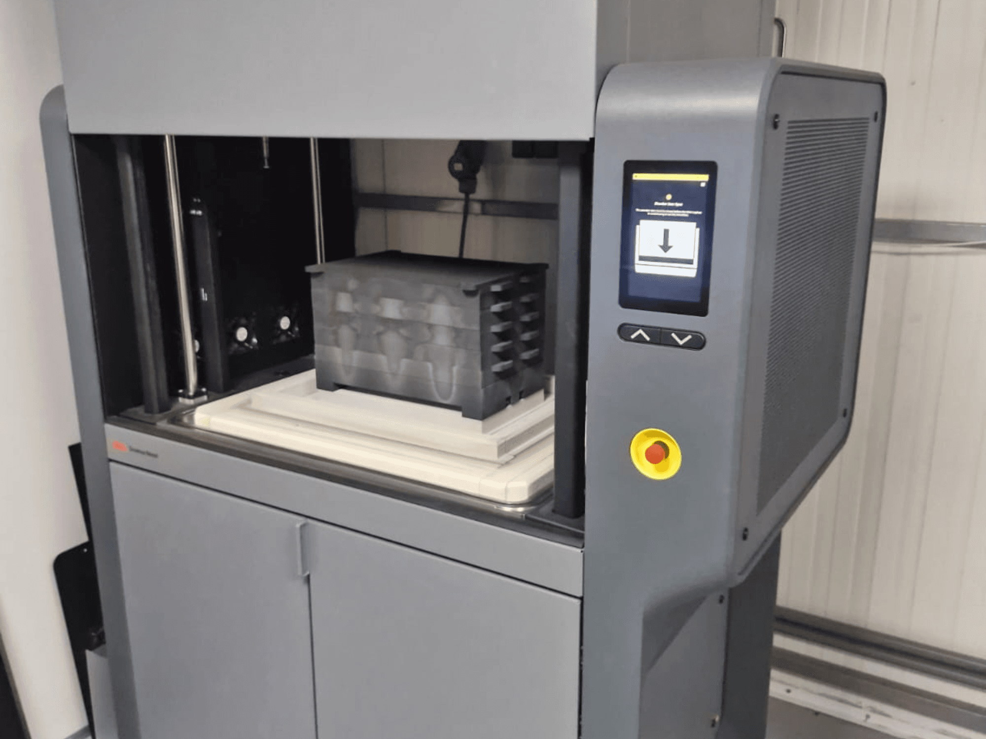 3D tiskárna Metal Studio 2 od společnosti Desktop Metal, pohled zepředu ukazuje ovládací panel a tiskové lůžko s černým kontejnerem.