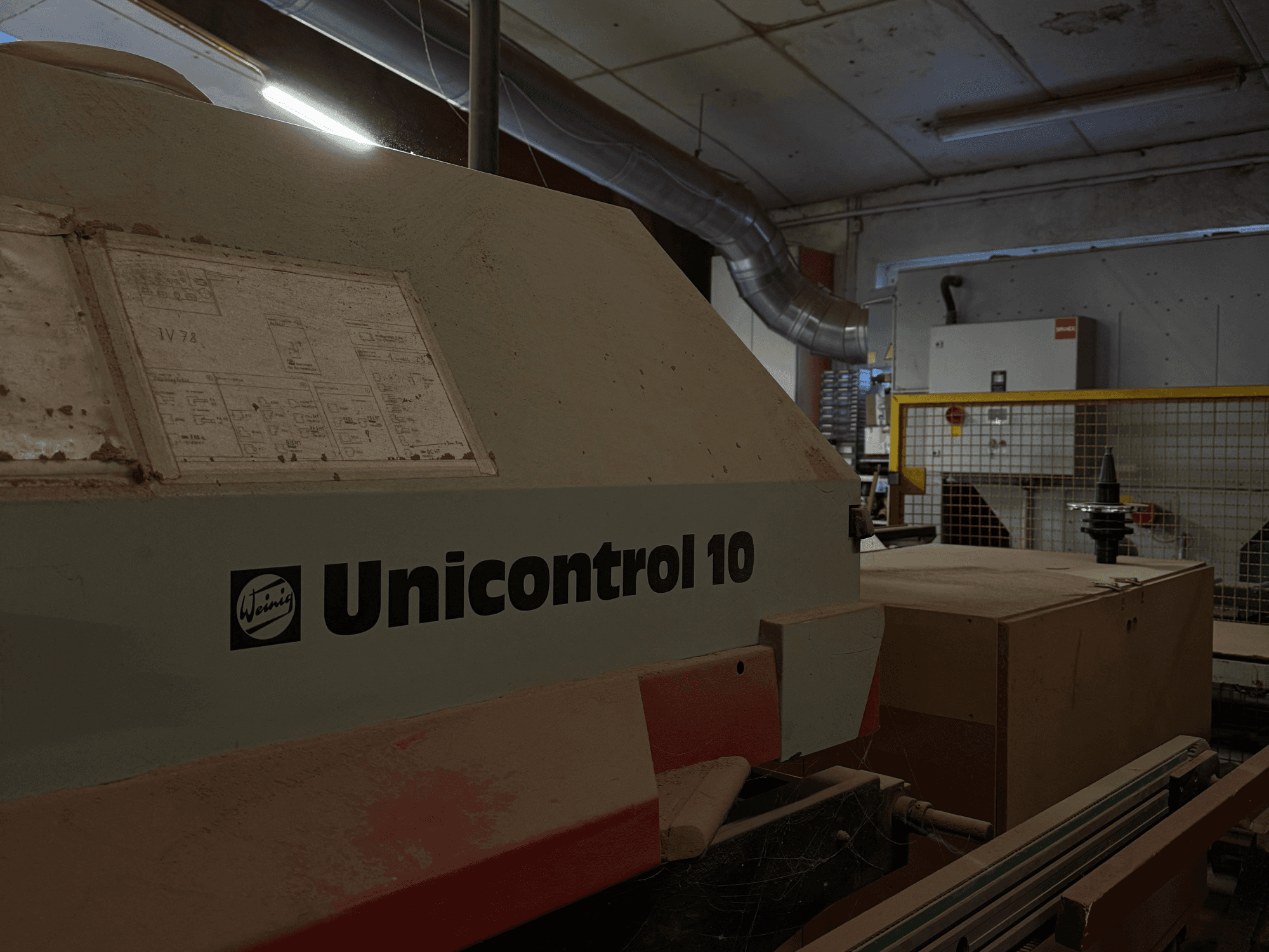 Stroj Weinig Unicontrol 10 z bočního pohledu, zaprášený povrch, na předním panelu viditelná technická schémata.
