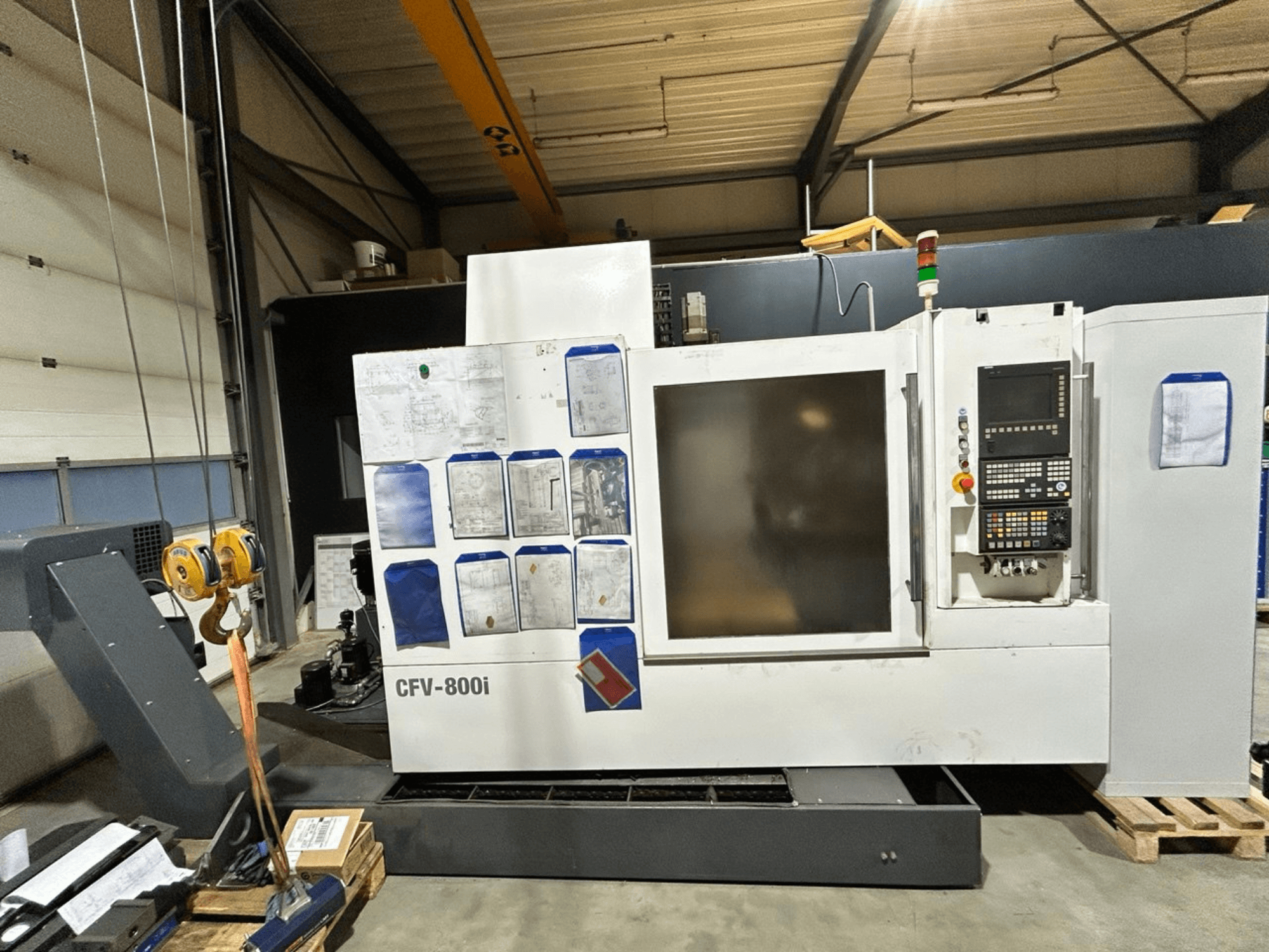 Stroj CFV-800i CNC zobrazený zepředu, s ovládacím panelem, dokumenty na boku a mostovým jeřábem v továrním nastavení.